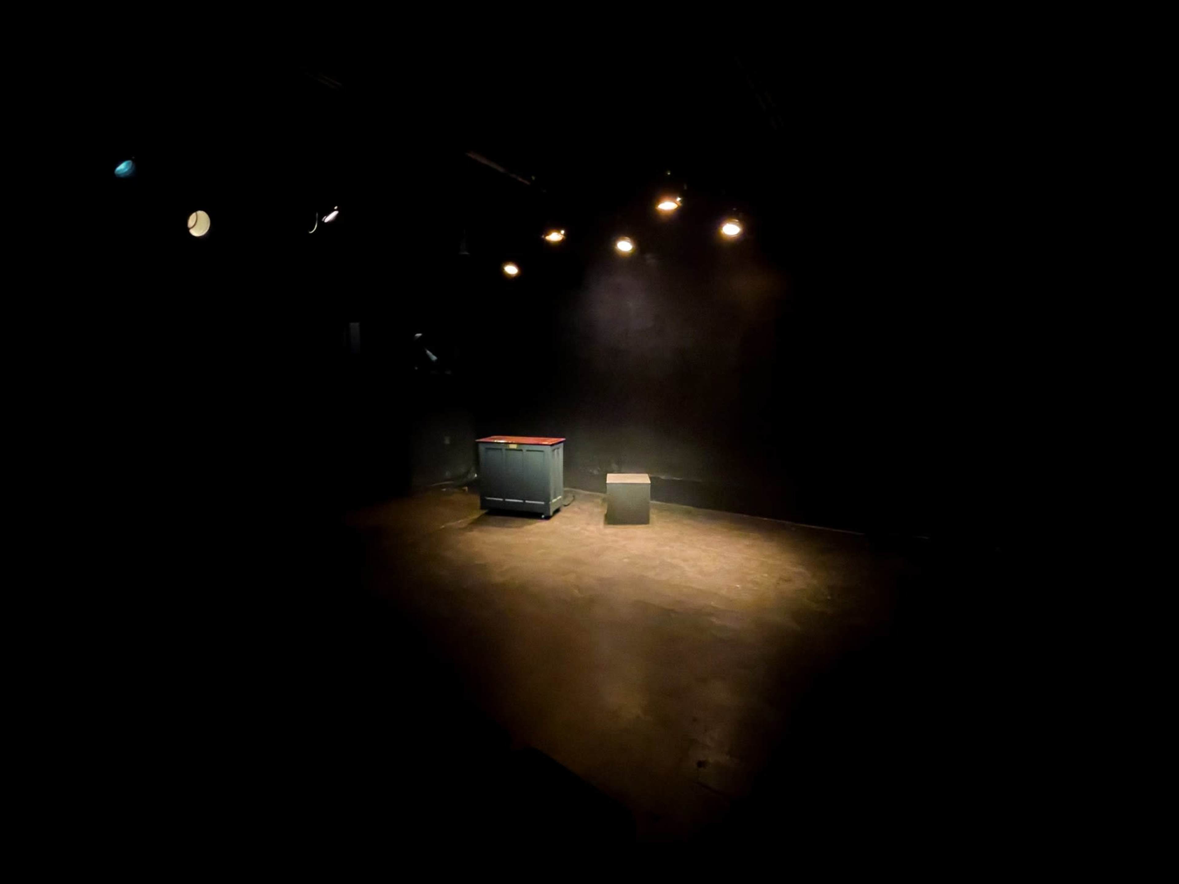 The scene features a dimly lit stage with a small table and a solitary box illuminated by overhead lights.