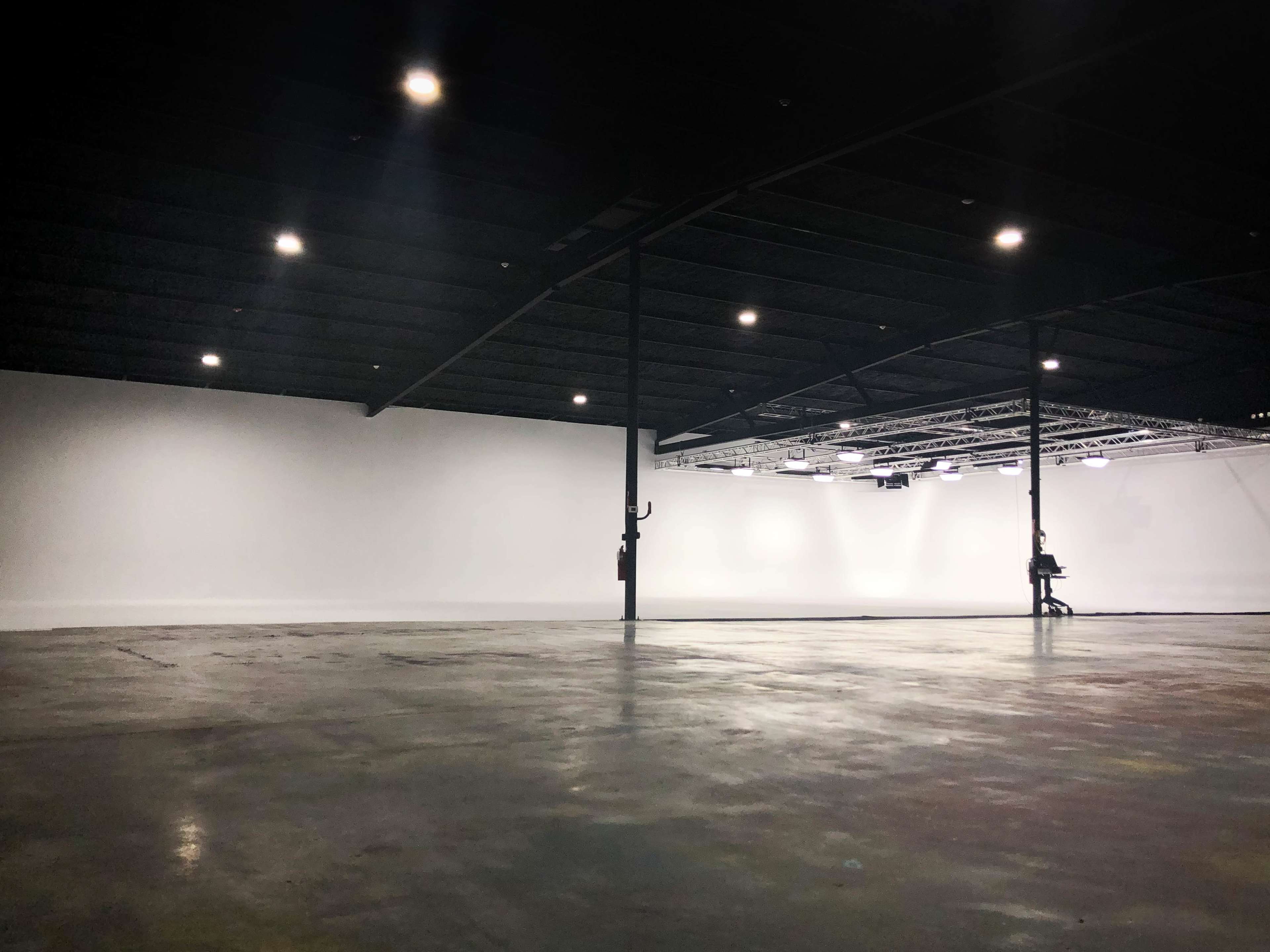 A large, empty industrial space with a concrete floor and high ceilings, illuminated by overhead lights.
