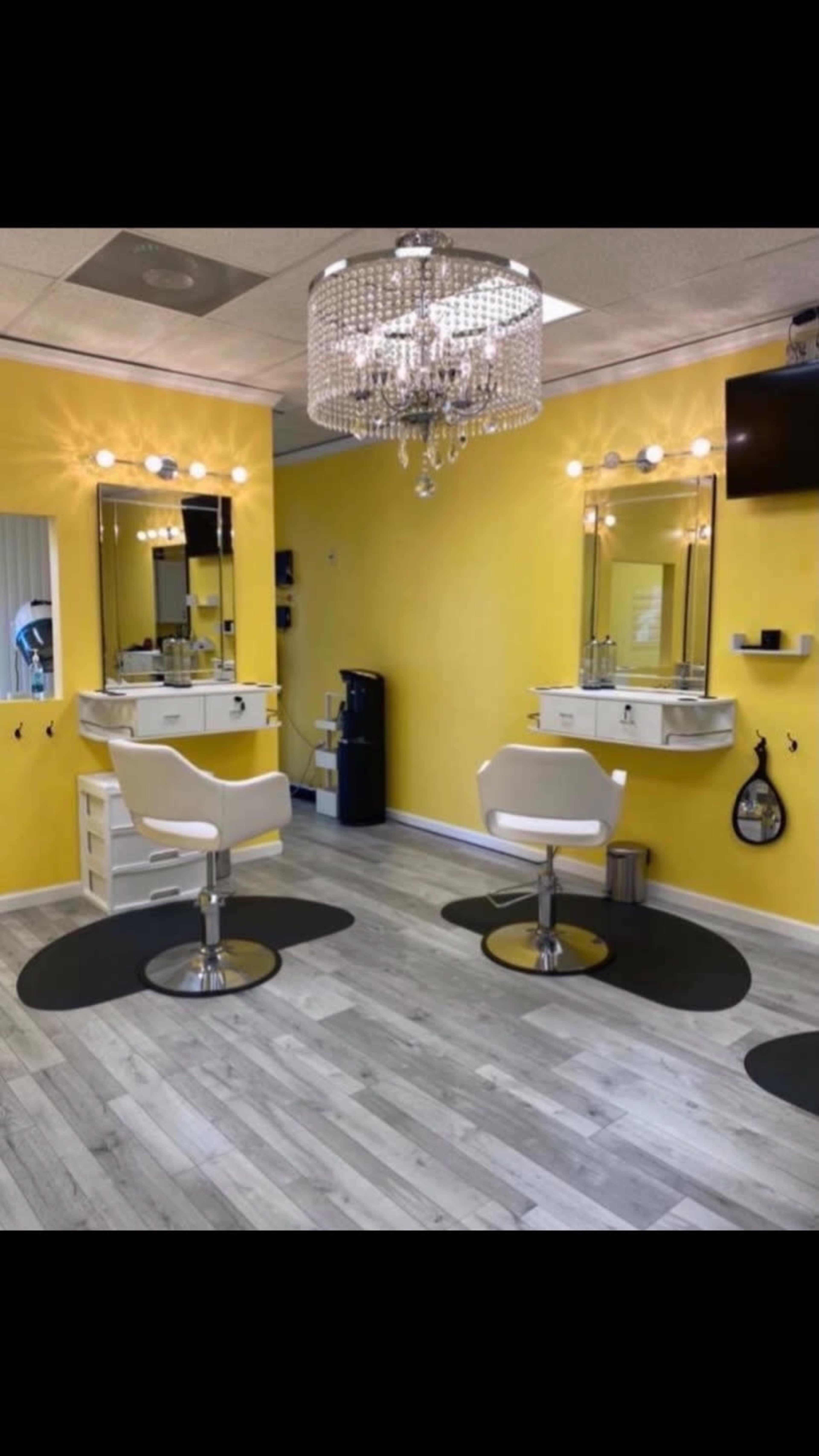 A bright yellow hair salon featuring two styling stations with mirrors, white chairs, and a chandelier.