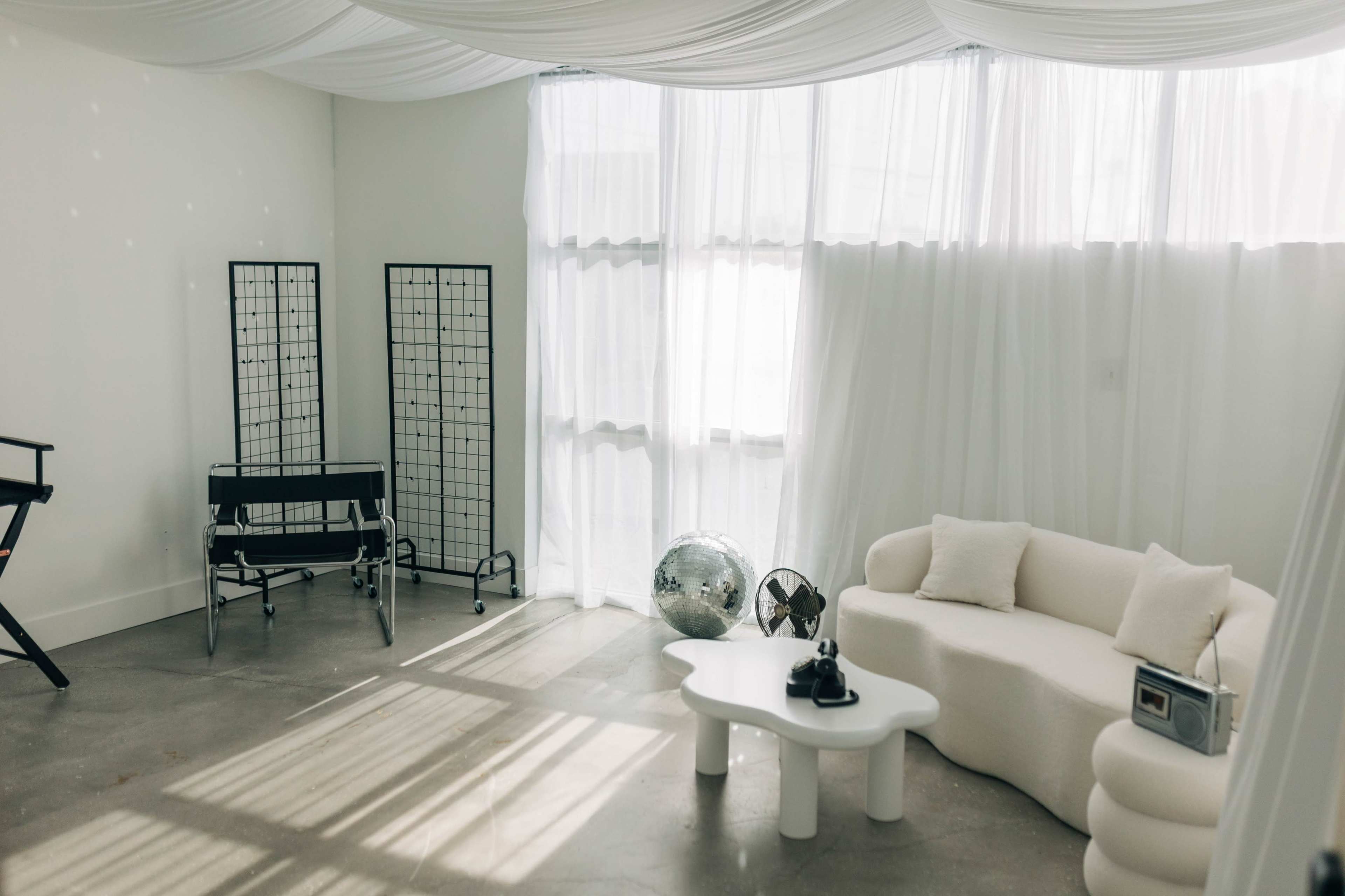The image shows a minimalist interior with a cozy white sofa, a round coffee table, a large globe, and light streaming through sheer curtains.