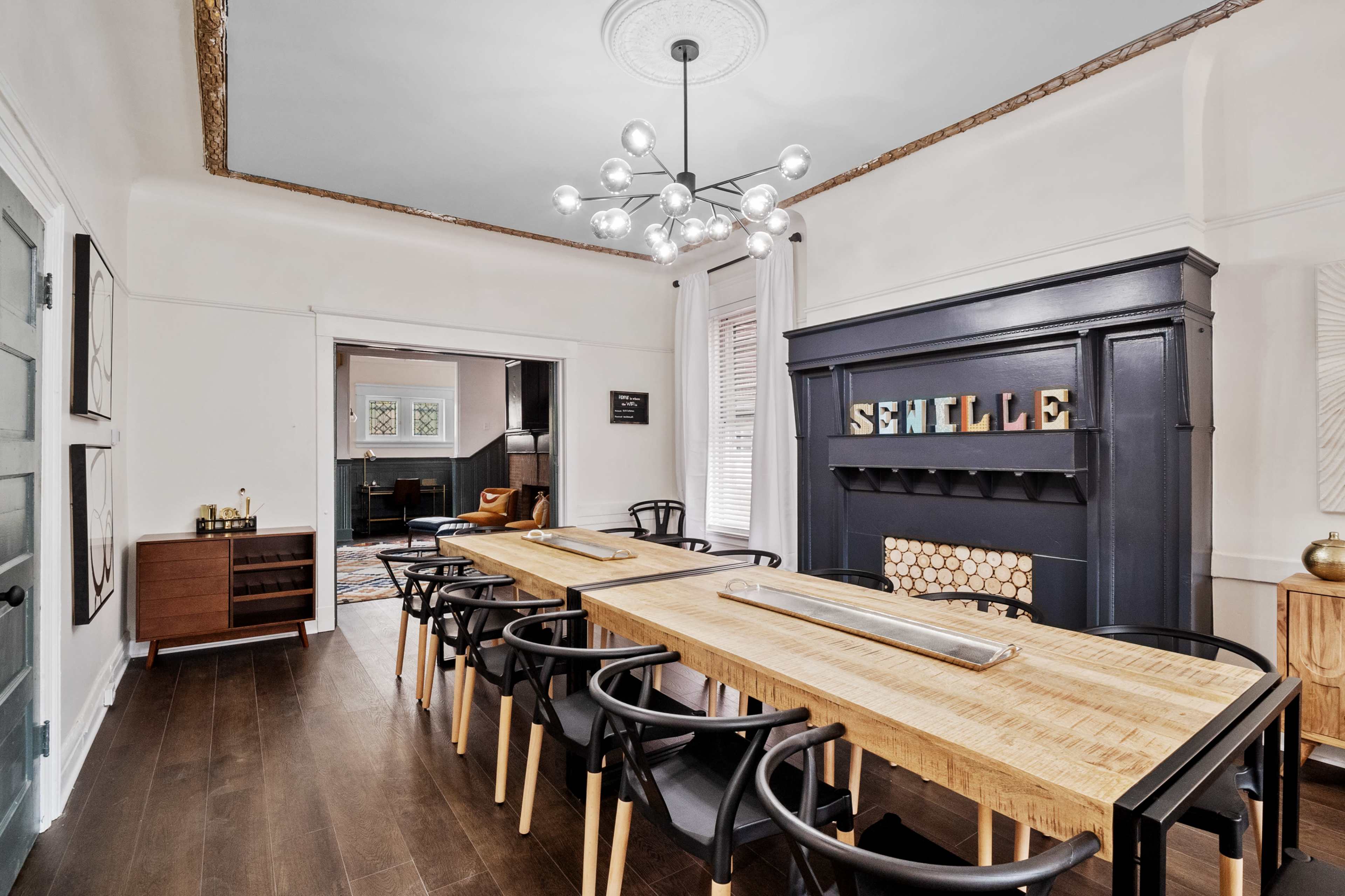 A modern dining room featuring a long wooden table with black chairs, a decorative fireplace with the word "Schnille" above it, and a stylish light fixture hanging from the ceiling.