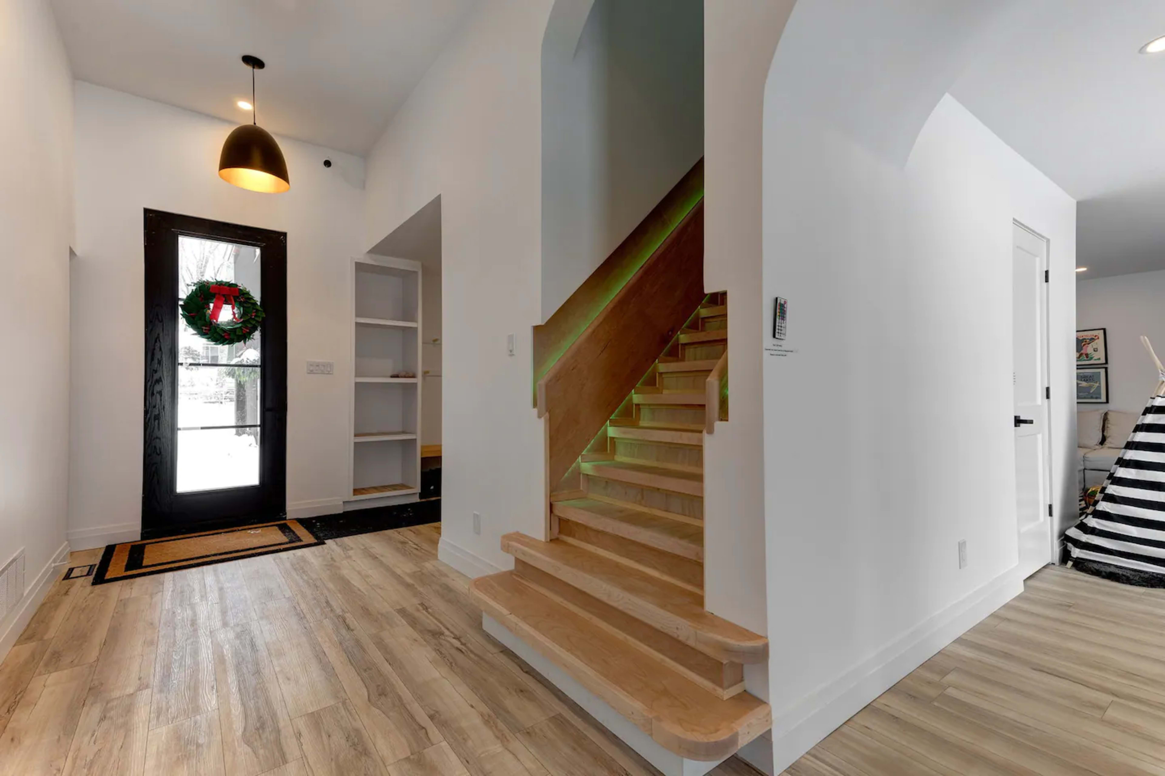 A modern foyer with a staircase on the right, a door at the front, and built-in shelves on the left.