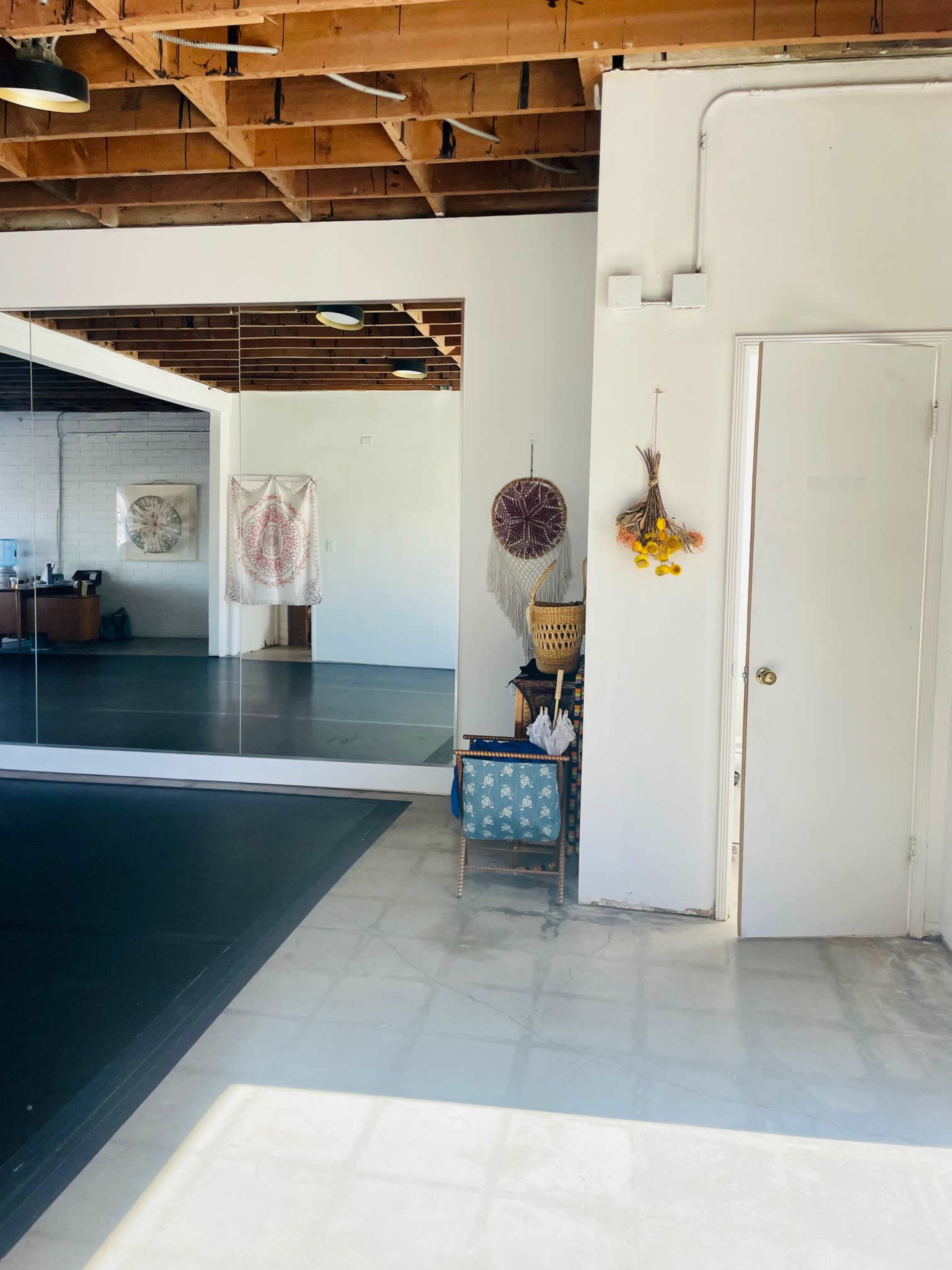 The image shows an interior space with a mirrored wall, a door, and decorative objects hanging on the wall, including tapestries and plants.