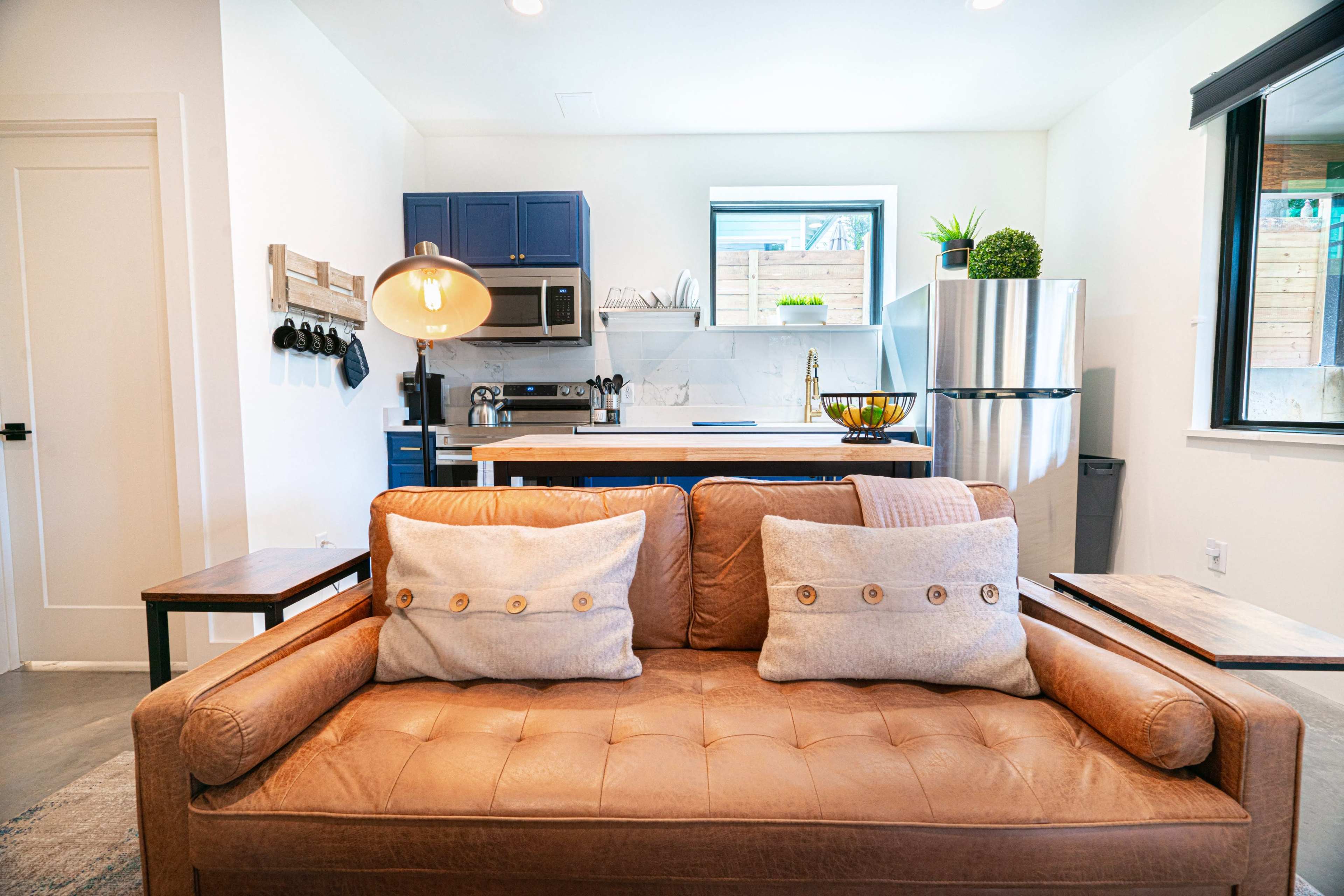 A brown leather sofa with two pillows is positioned in the foreground of a modern kitchen featuring blue cabinets and stainless steel appliances.