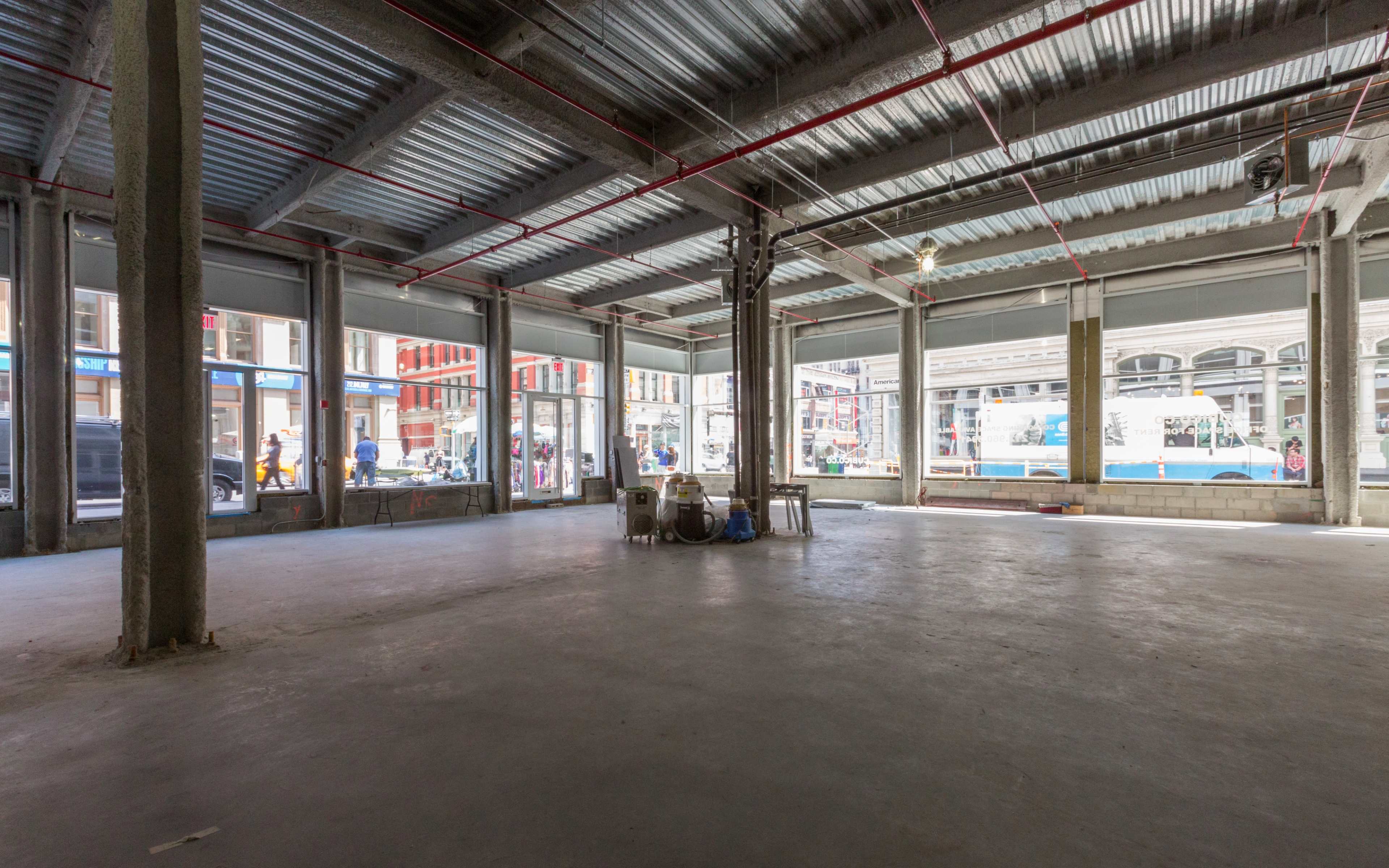 An empty industrial-style space with large windows and visible structural elements, including metal beams and concrete flooring.