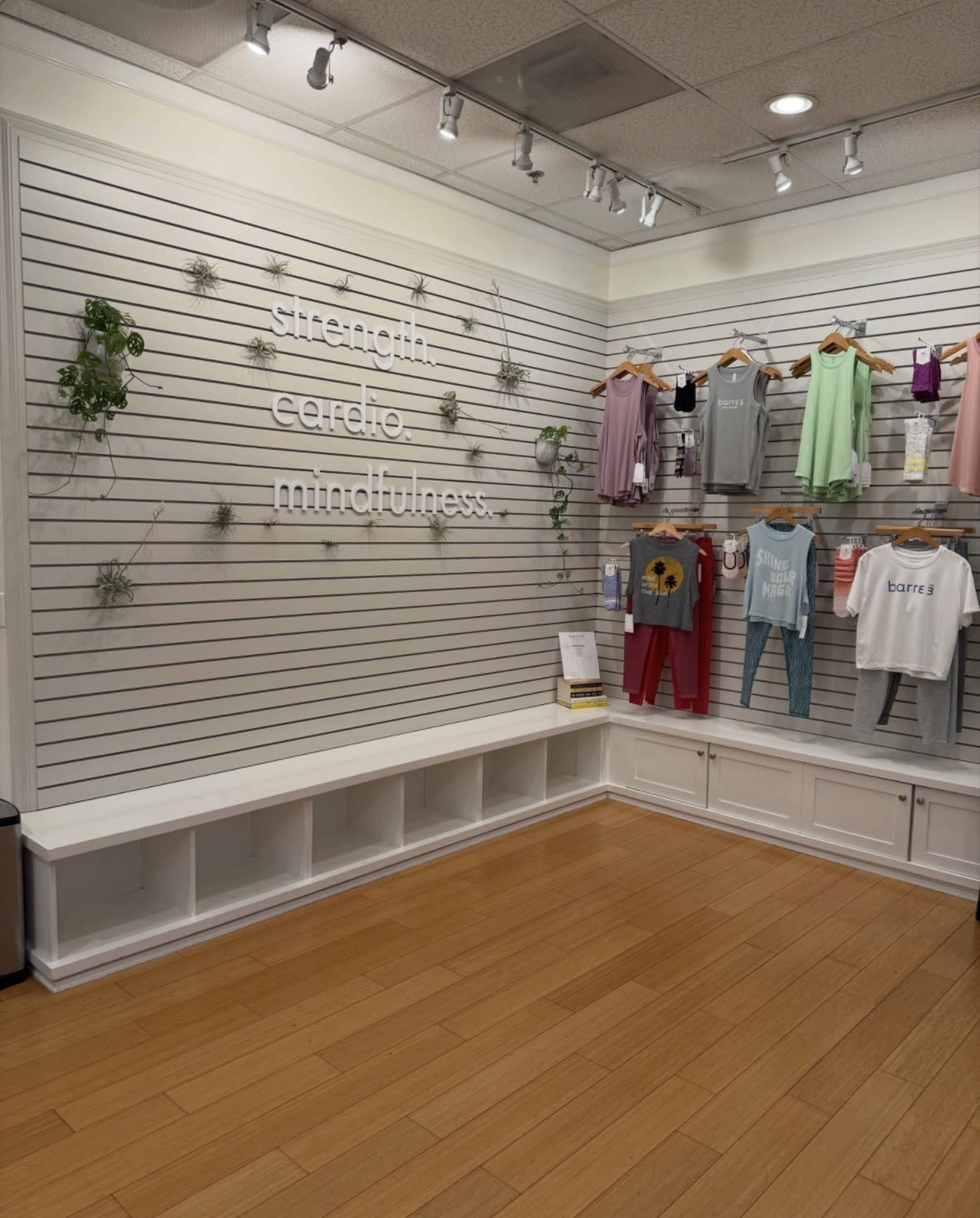 The image shows a retail store interior featuring a wall with the words "strength, cardio, mindfulness" decoratively arranged above a display of colorful clothing on hangers.