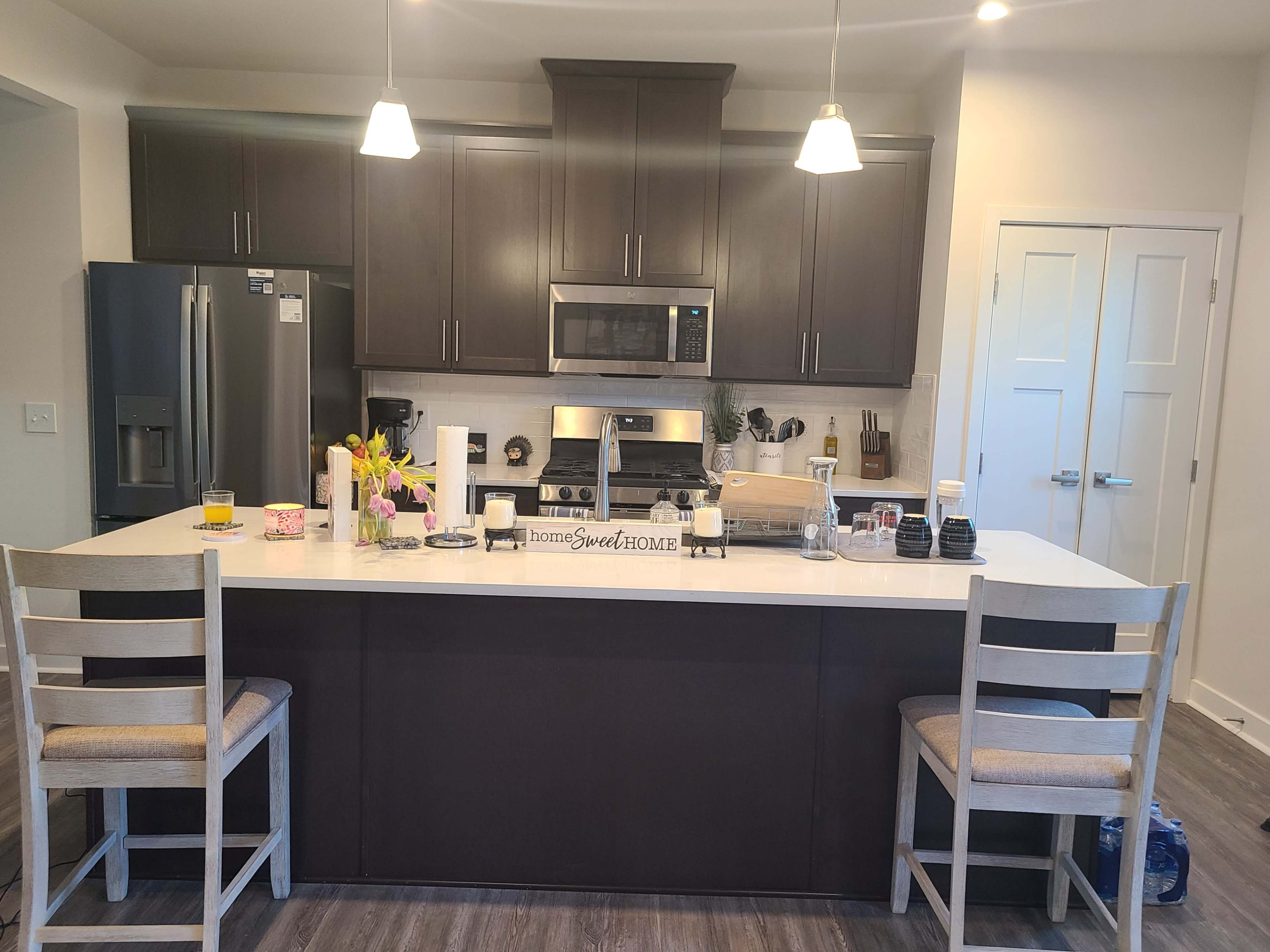 A modern kitchen featuring dark cabinetry, a central island with two chairs, and stainless steel appliances.
