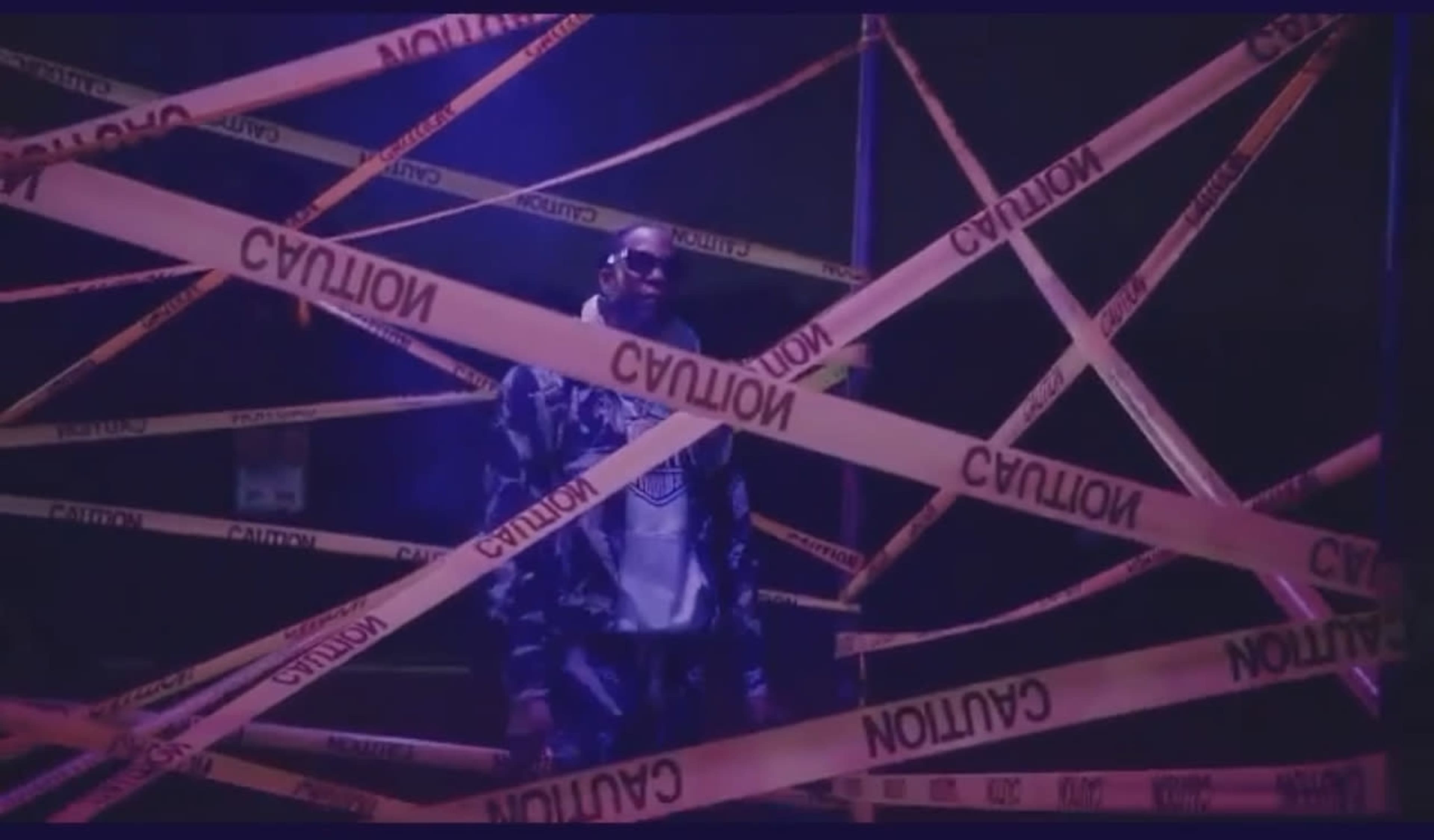 A person stands surrounded by orange caution tape in a dimly lit area.