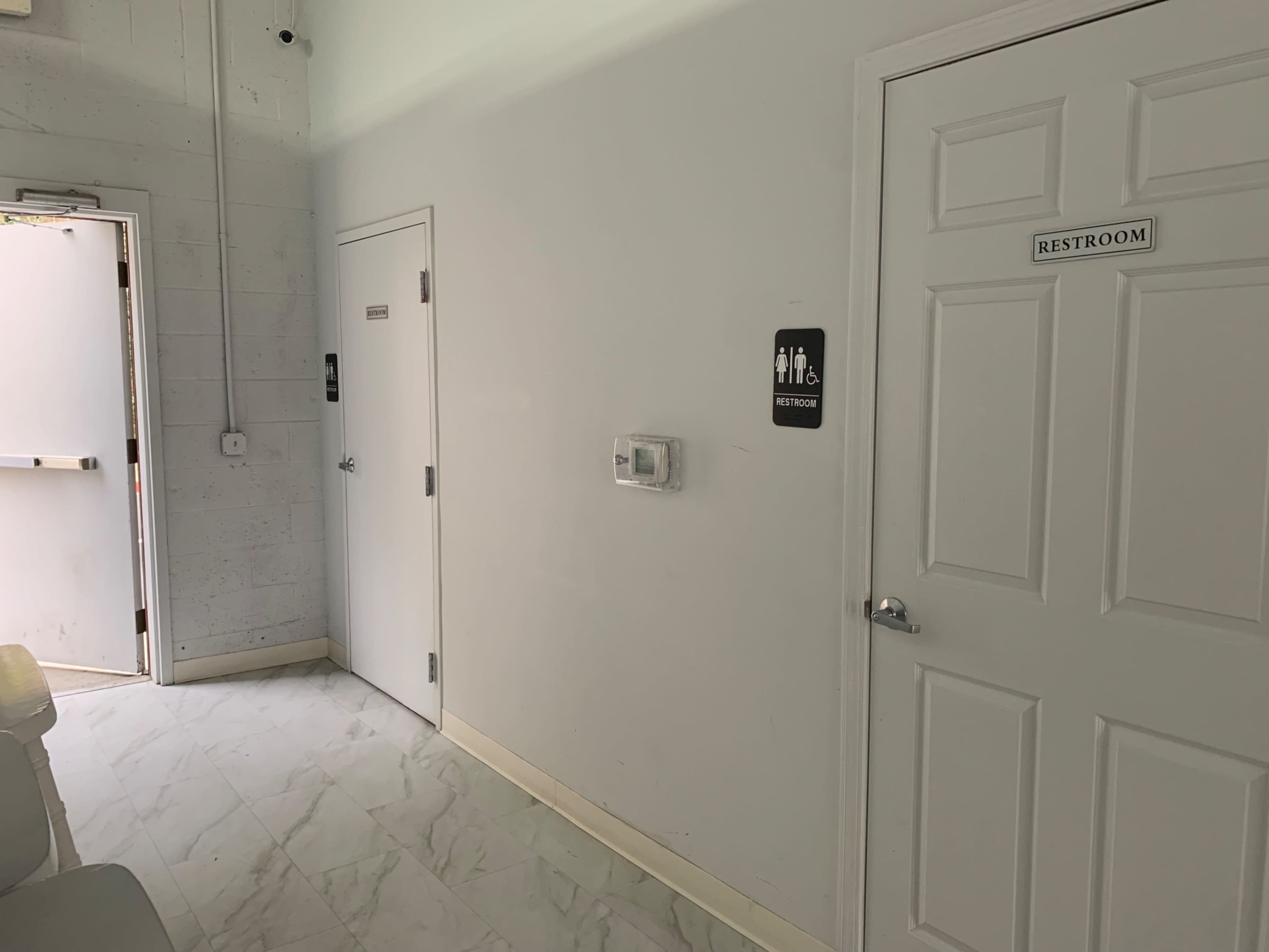 A clean, white corridor with two doors labeled for restrooms, one on the right and another on the left, and an exit door at the far end.