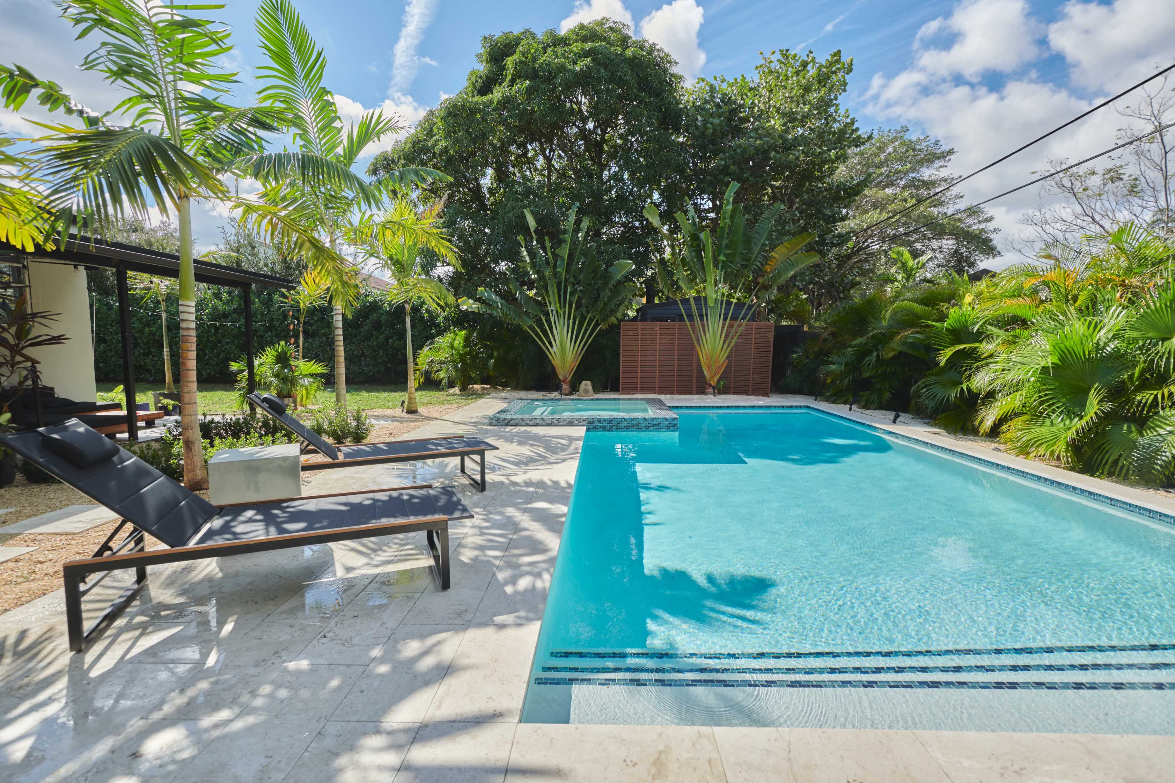 A modern swimming pool surrounded by tropical plants and lounge chairs in a residential backyard.