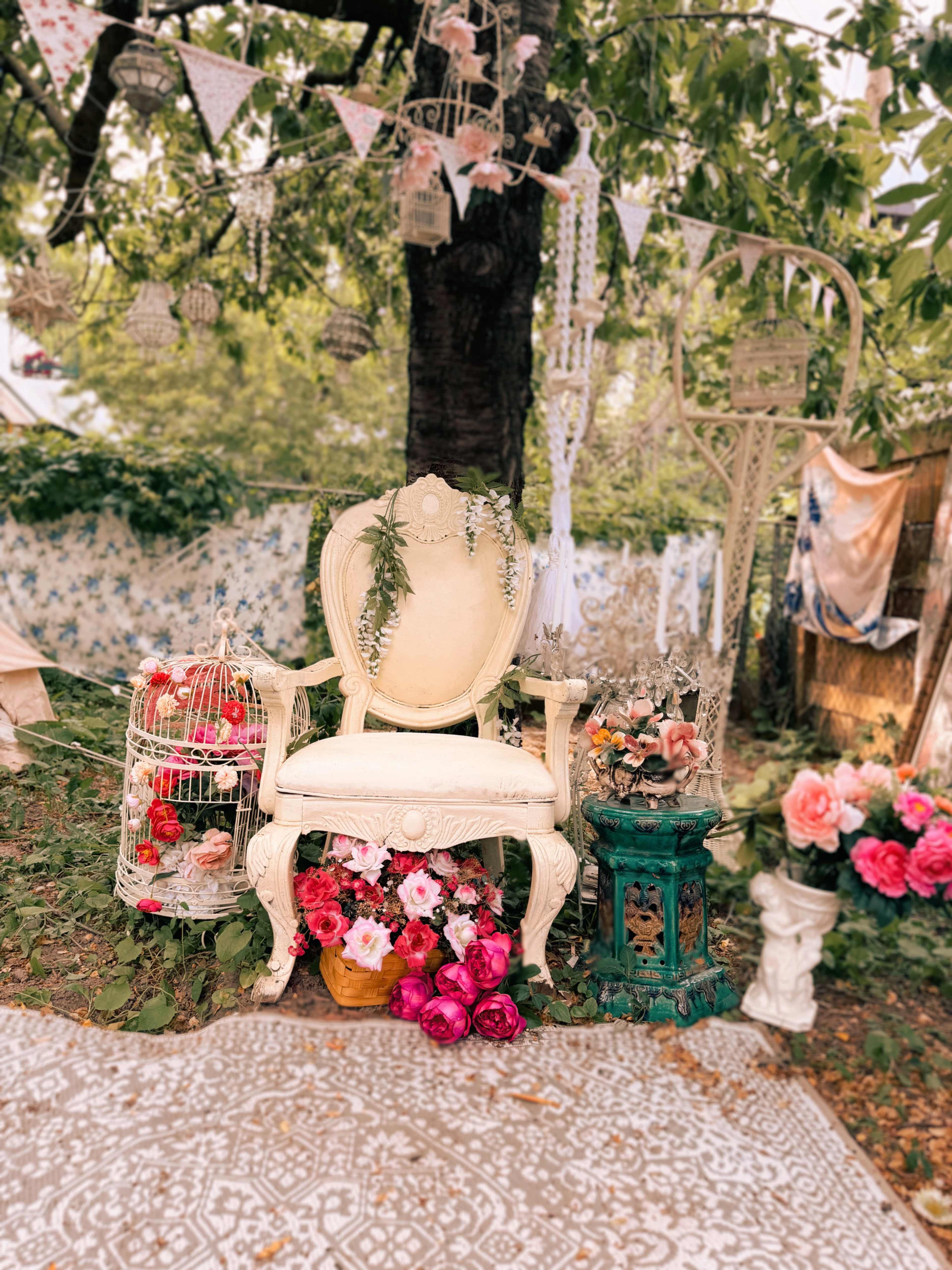 The scene features an elegantly designed white chair surrounded by colorful flowers, decorative items, and a tree adorned with banners.