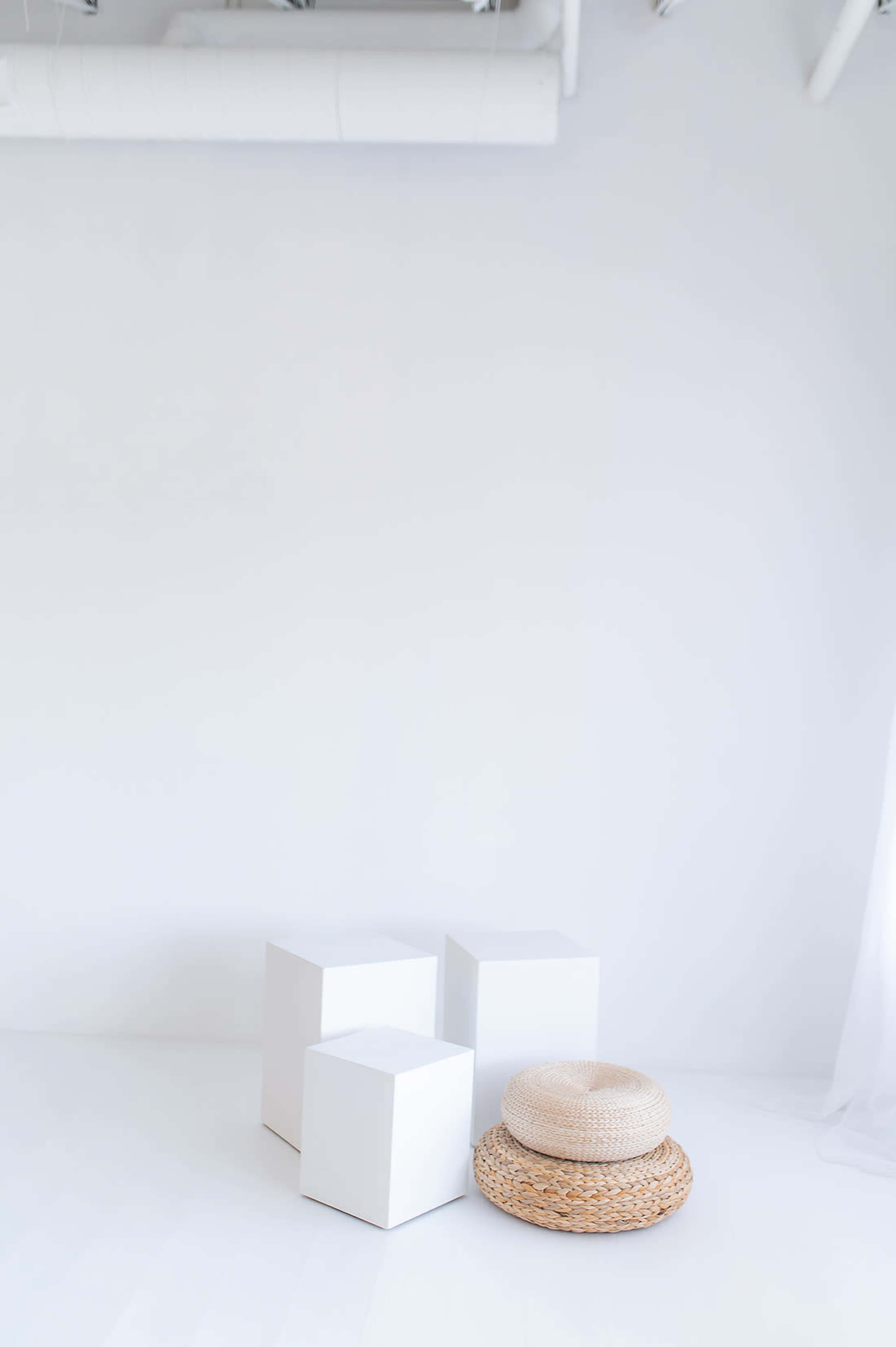 The image features three white cubes and a straw hat on a light-colored floor against a plain white wall.
