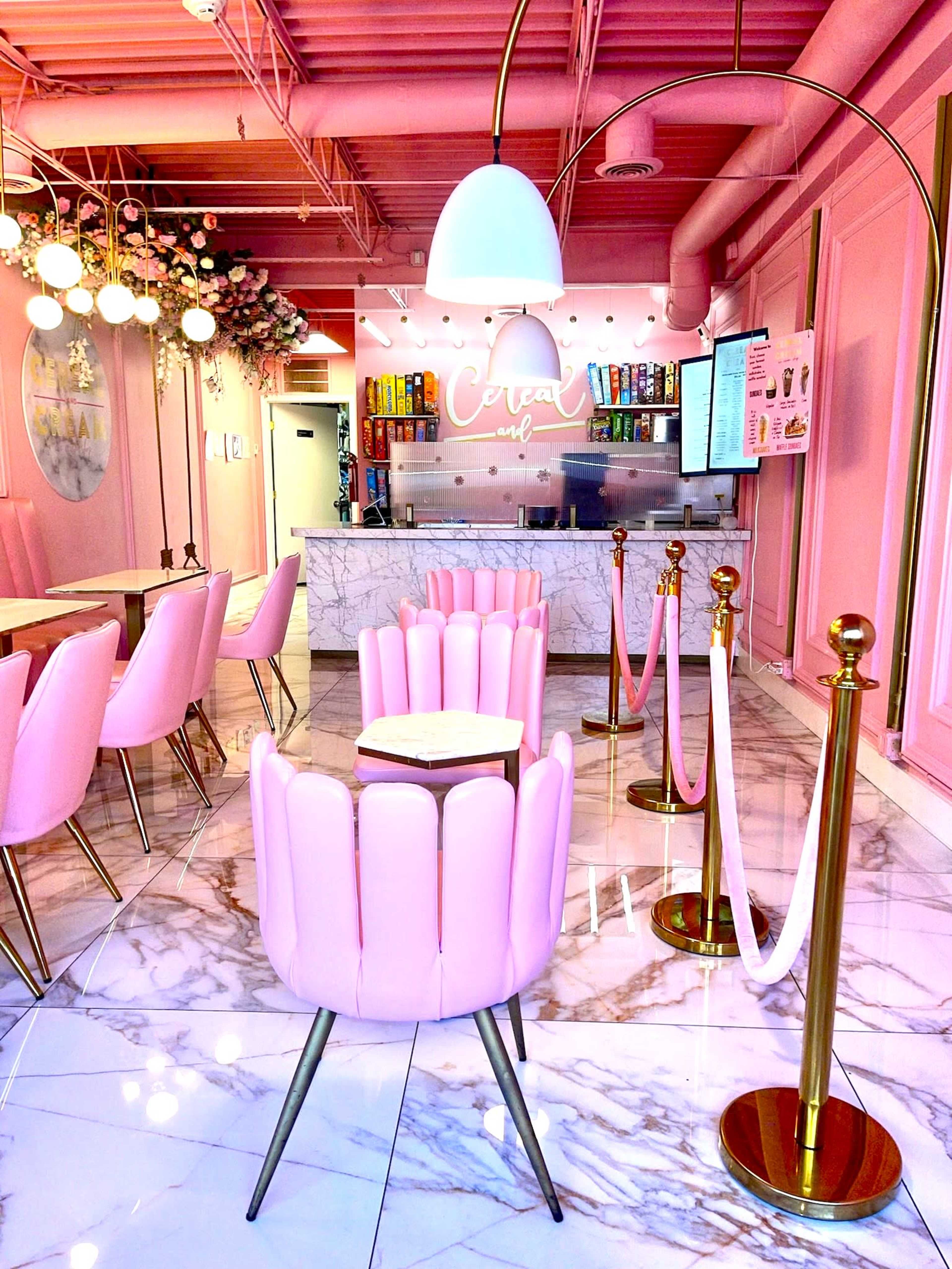 A brightly colored café with pink decor, featuring flower arrangements, marble countertops, and stylish seating.