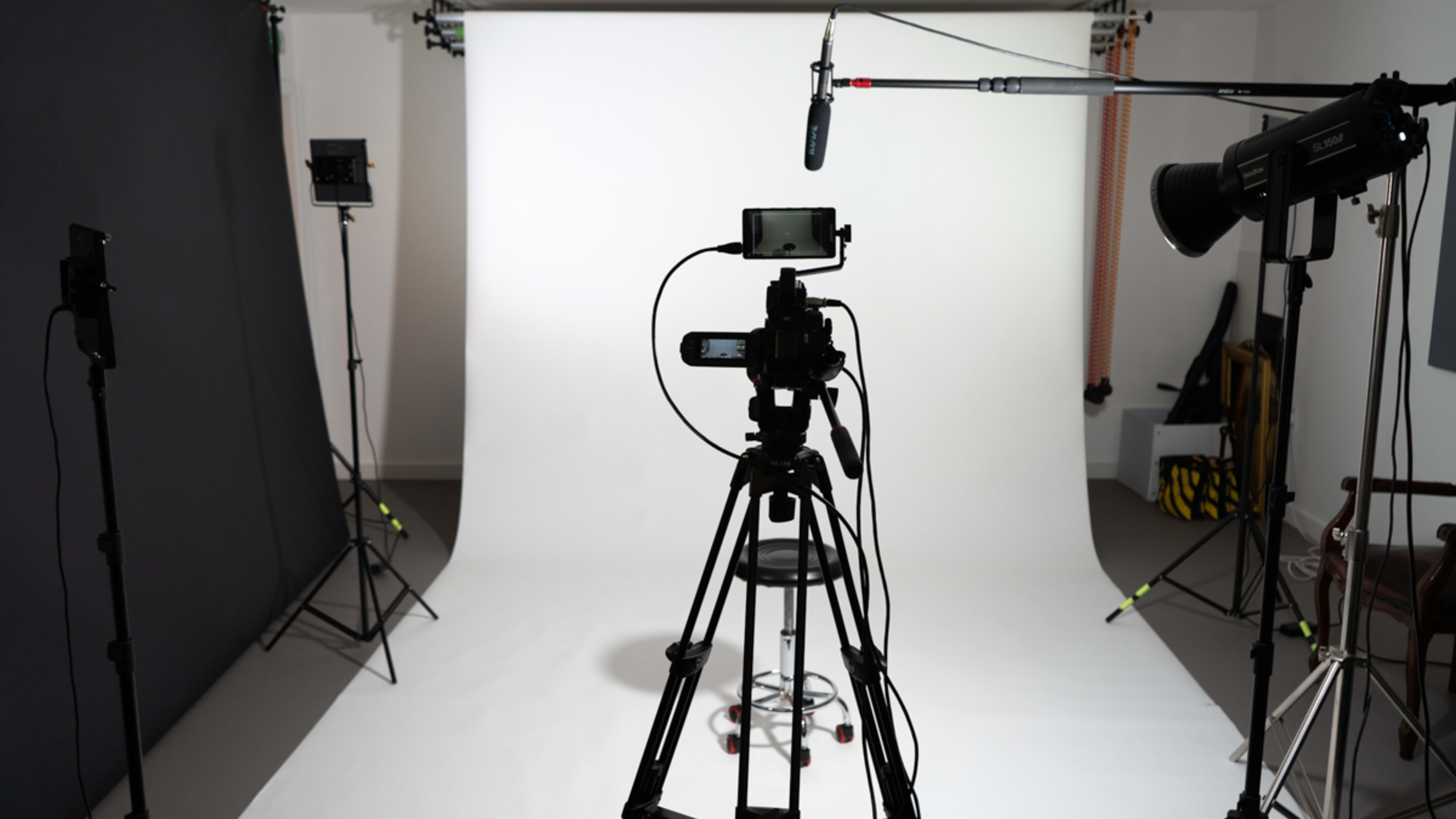 A camera and microphone setup are positioned facing a blank white backdrop in a photography studio.