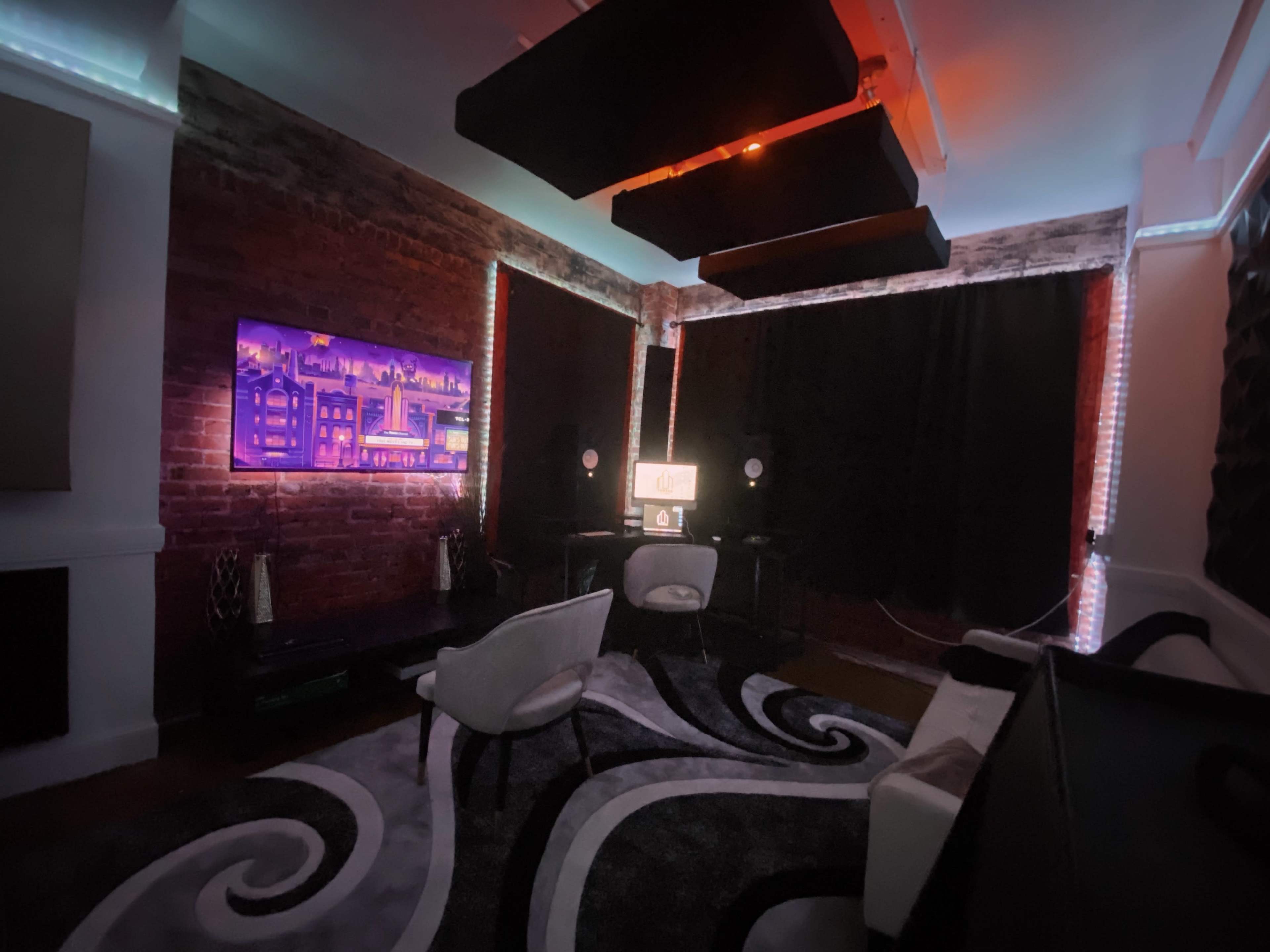 A modern room with exposed brick walls, dark curtains, a patterned rug, and contemporary furniture, illuminated by colored lights.