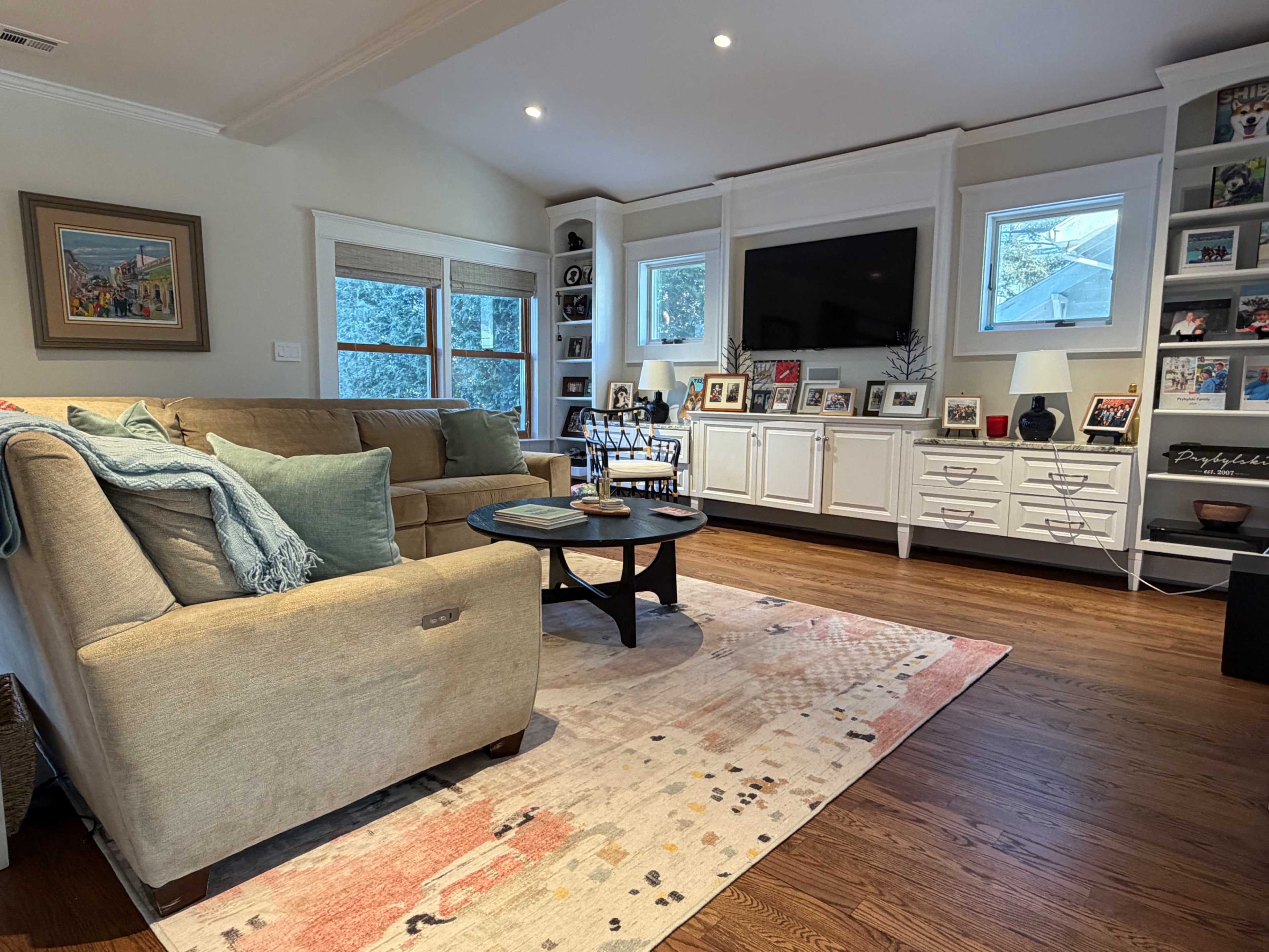 The living room features a beige sofa, a round coffee table, and a built-in bookshelf with framed photographs and decorative items.