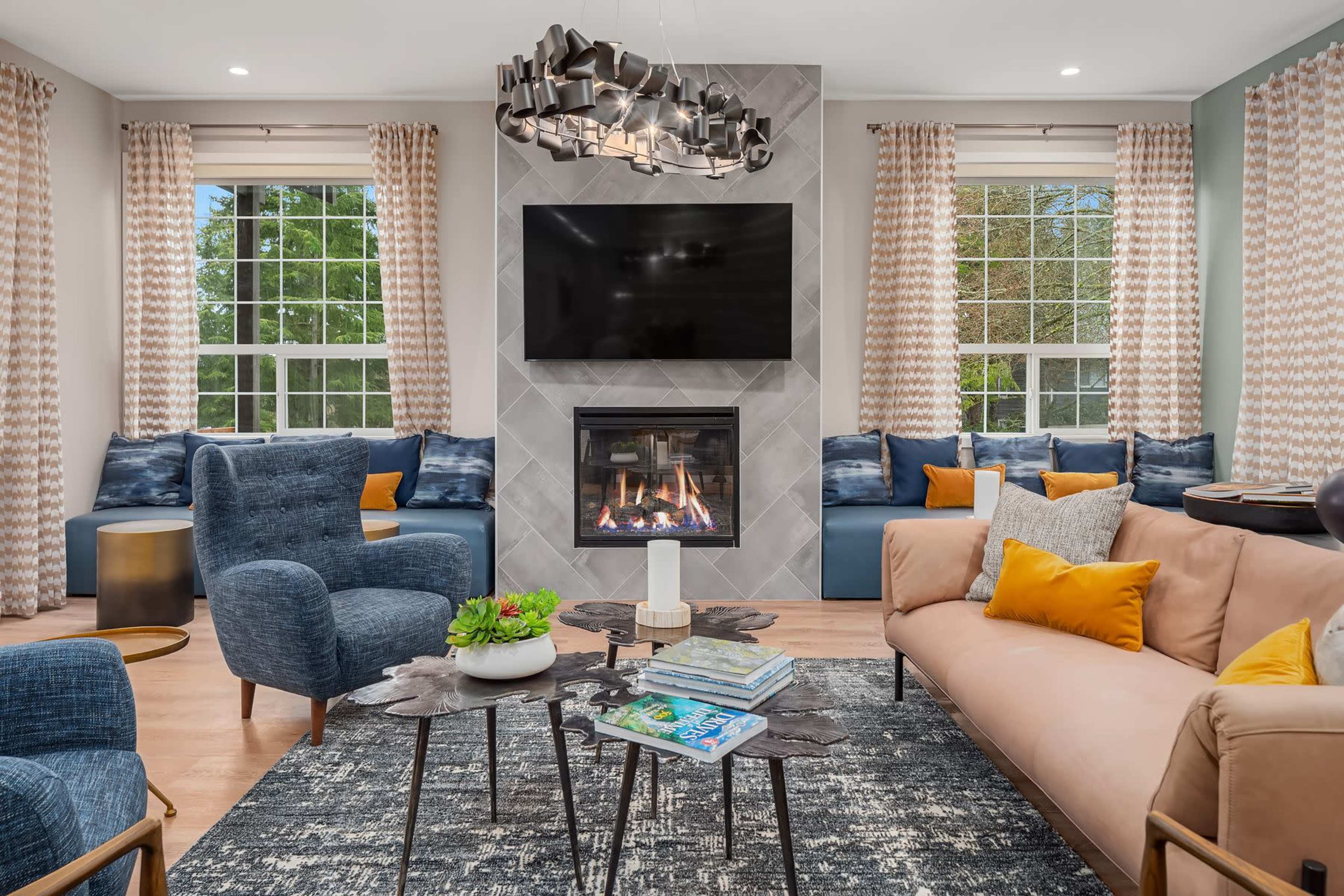 The living room features a fireplace set against a tiled wall, with a large television above it, surrounded by seating that includes a beige sofa and blue chairs.
