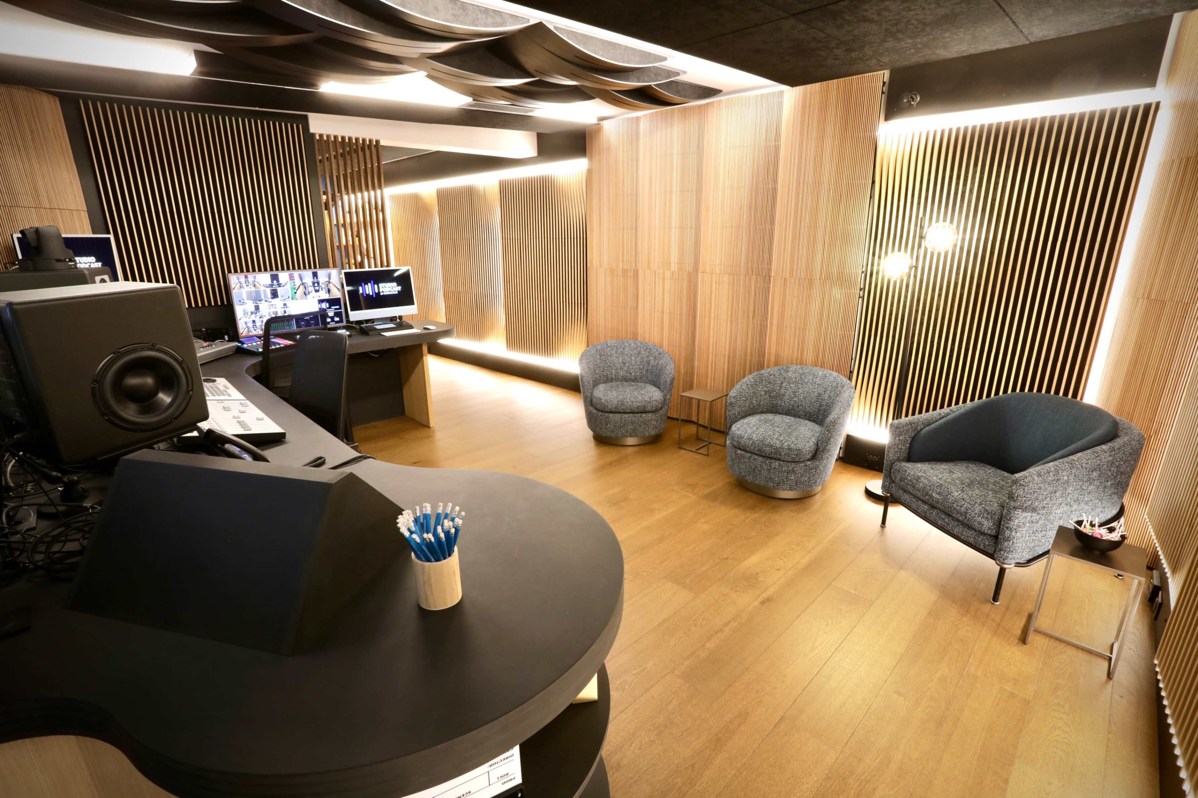 A modern studio interior with wooden paneling, a sleek black desk, and two gray armchairs arranged in a well-lit space.