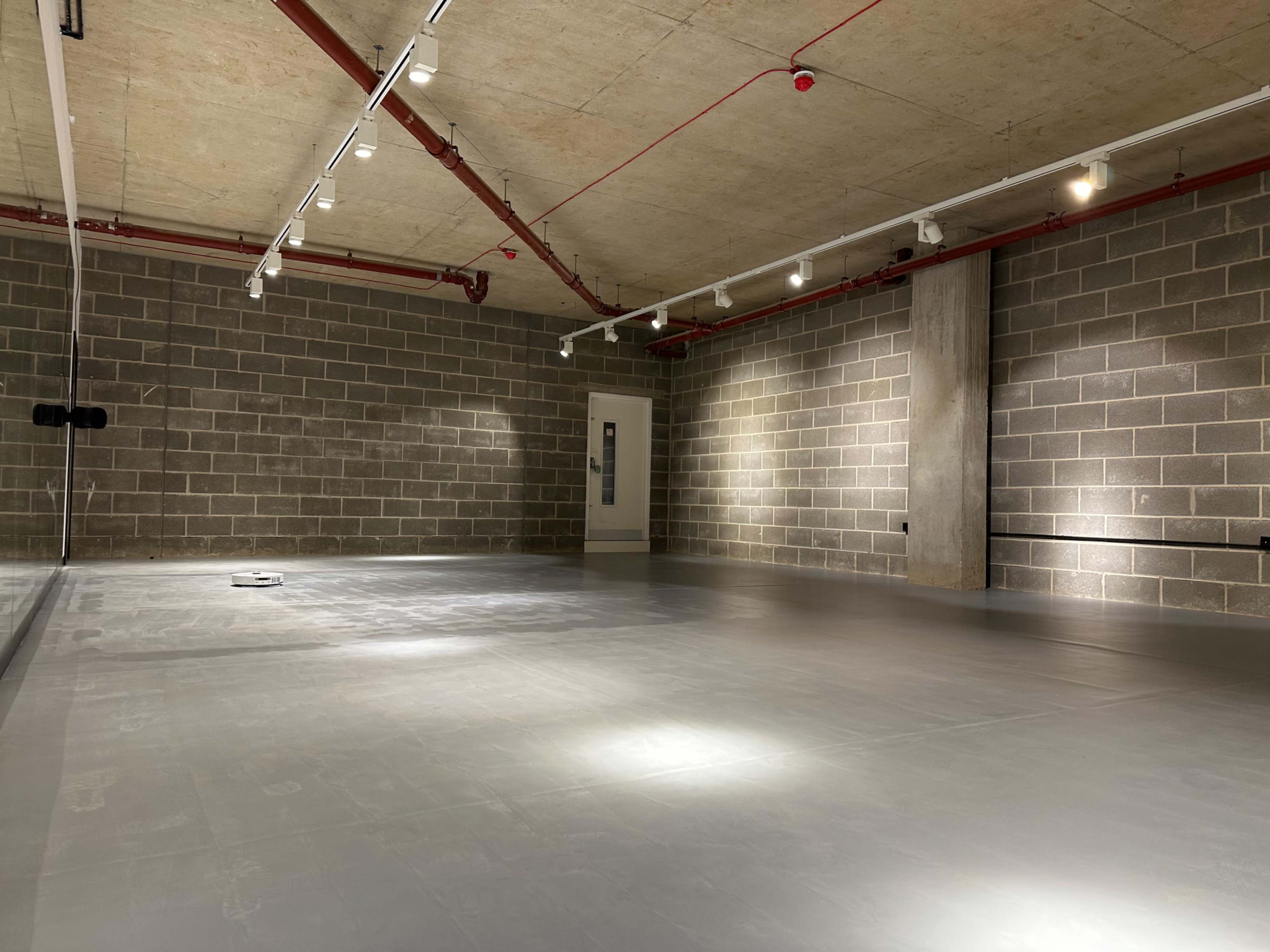 The image shows a spacious, empty room with concrete walls, a smooth floor, and industrial lighting.