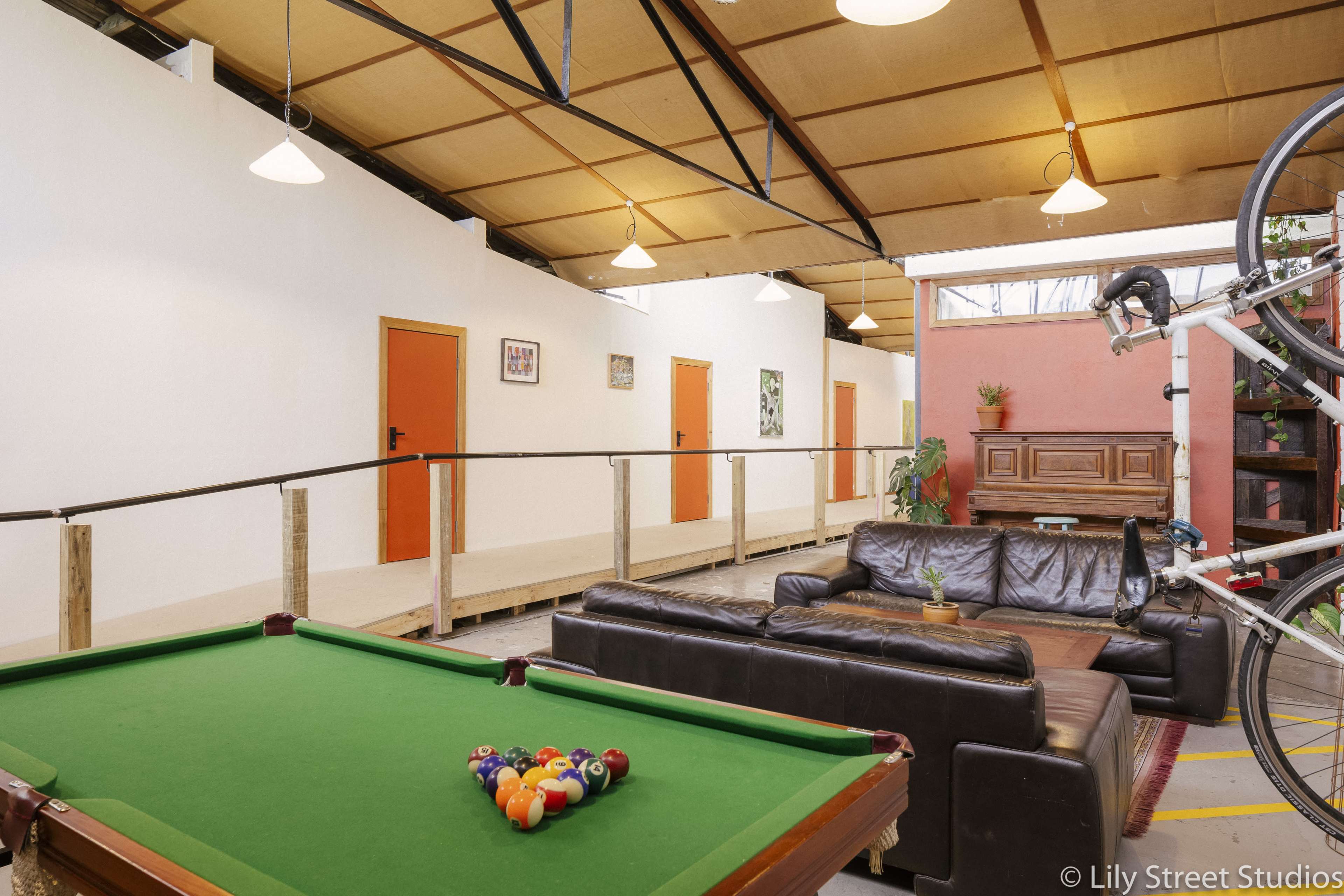 The image shows a spacious indoor area featuring a green pool table, a leather sofa, and brightly colored doors along the walls.