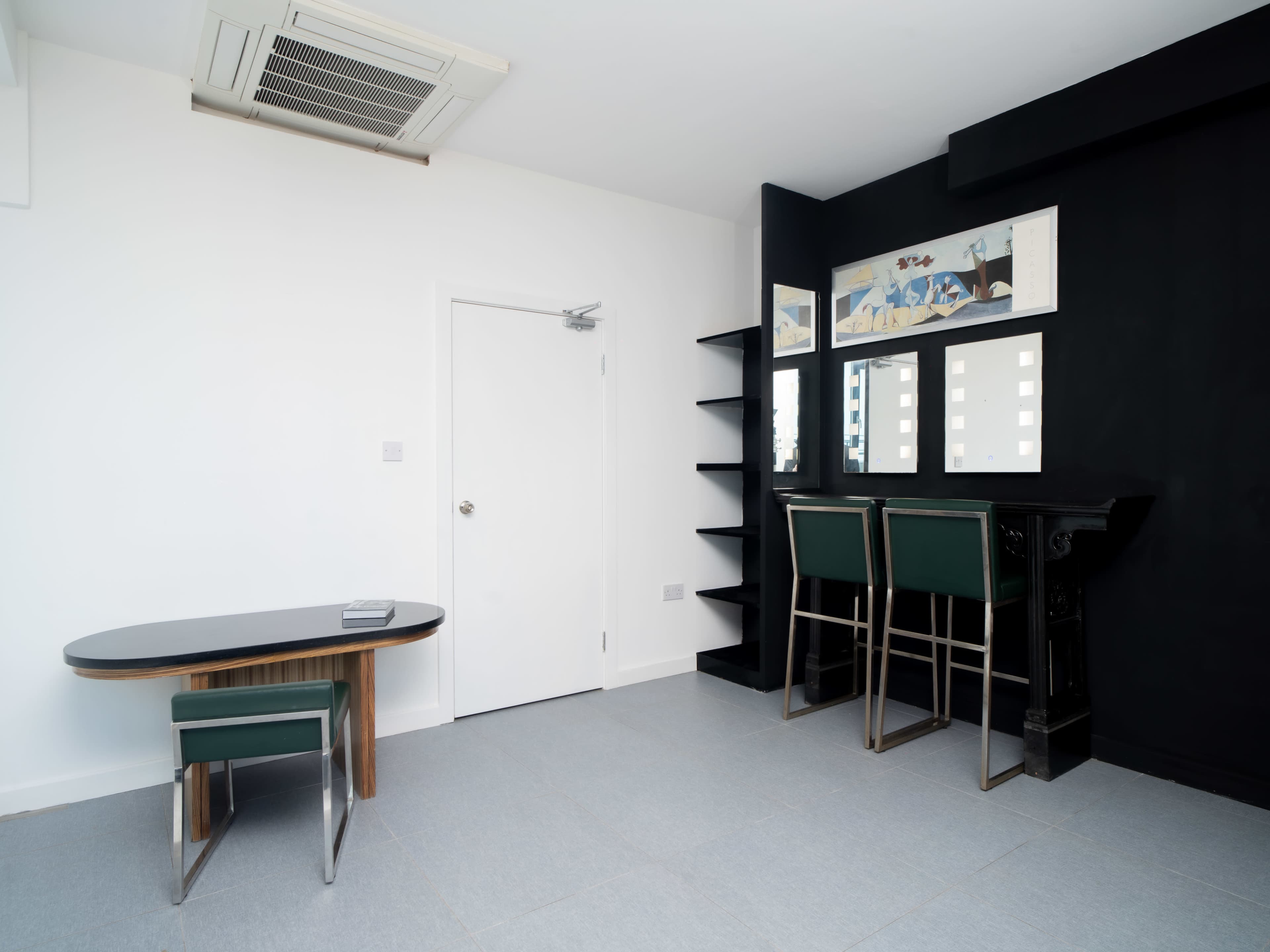 The image shows a minimalist room with a small table, a chair, a door, open shelves, and a bar-style seating area against a black wall.