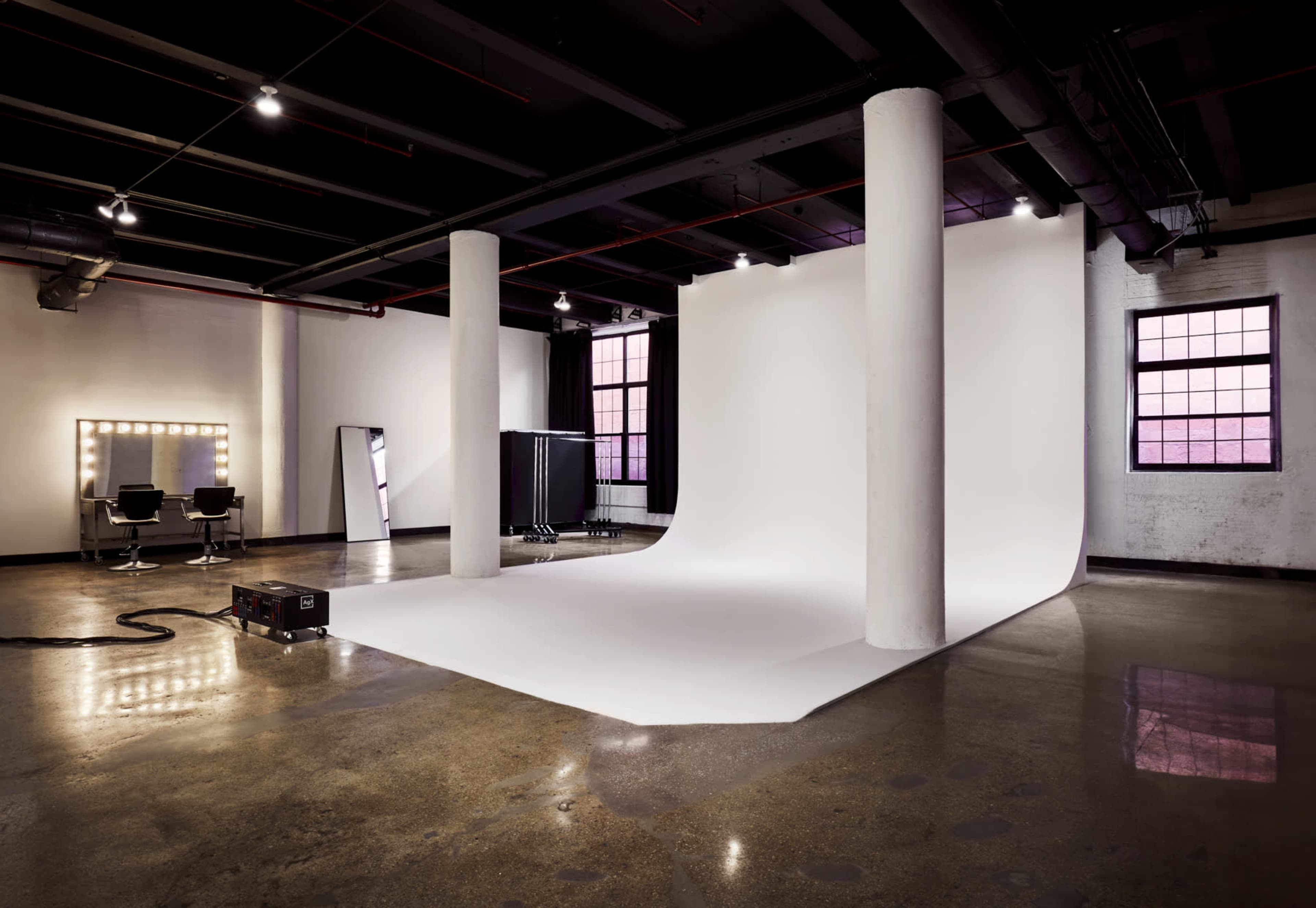 The image shows a spacious photo studio with a white backdrop, large mirror, and two hairstyling chairs.