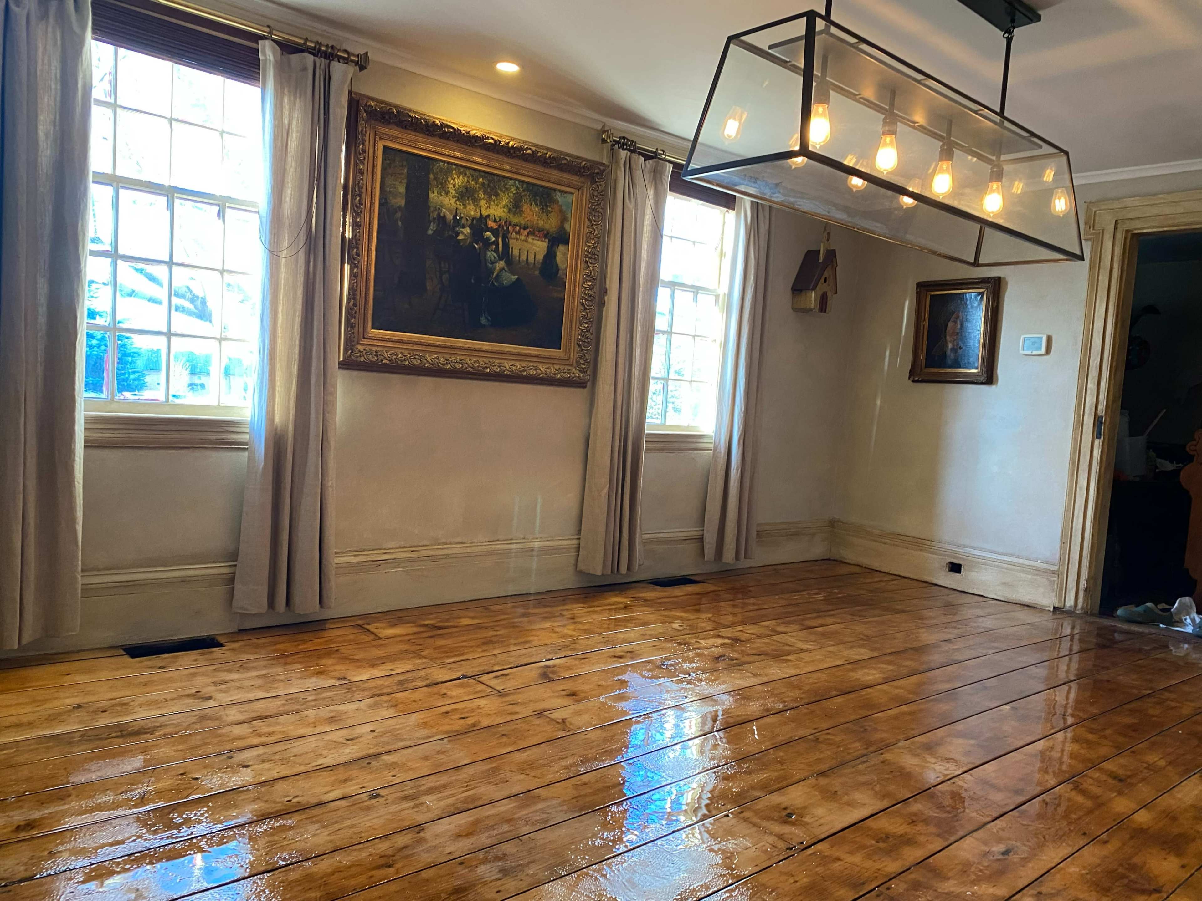 The room features a polished wooden floor, large windows, and a modern light fixture hanging from the ceiling, complemented by classical artwork on the walls.