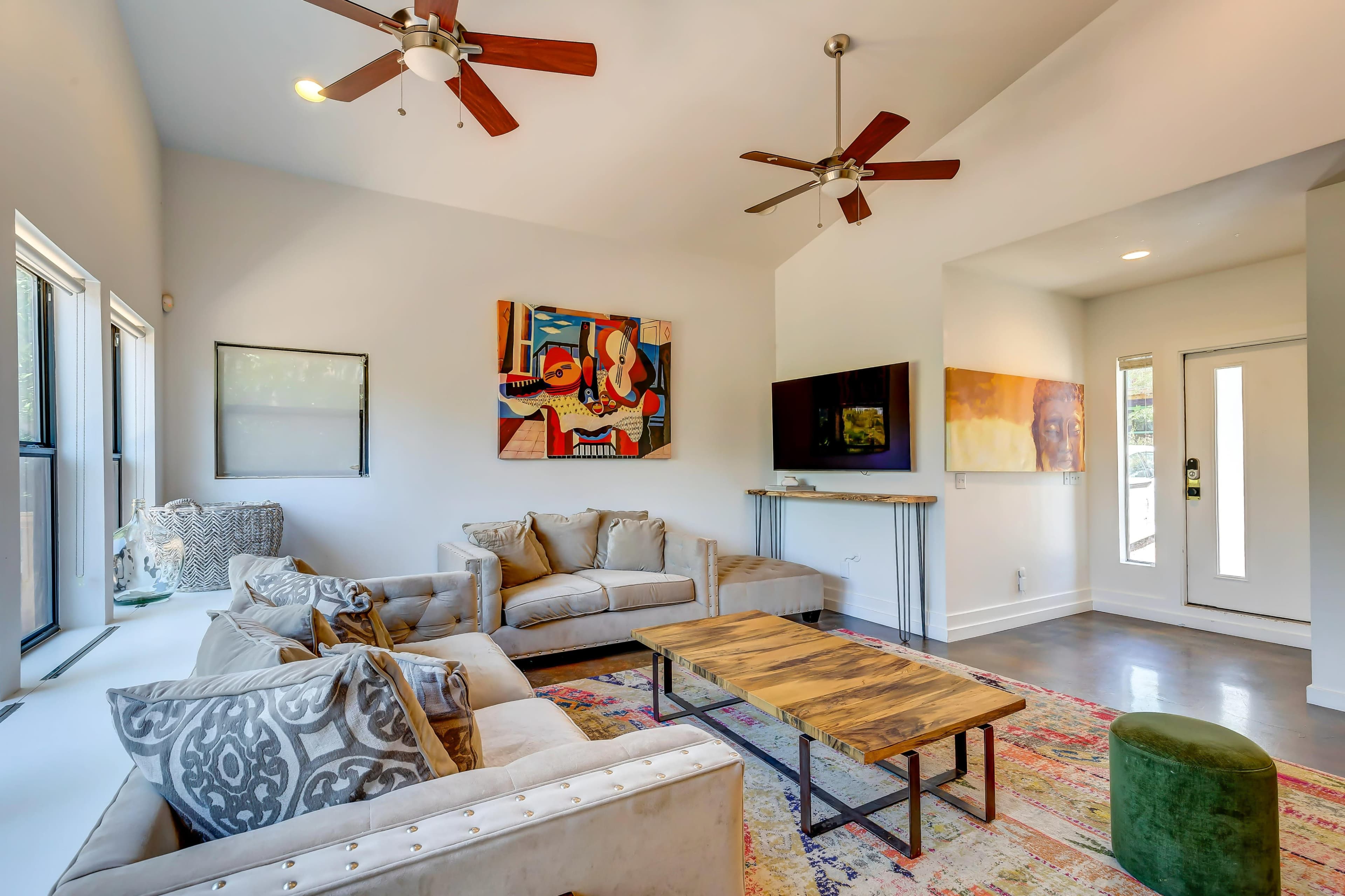 A modern living room with a sofa, a wooden coffee table, two ceiling fans, and artwork on the walls.