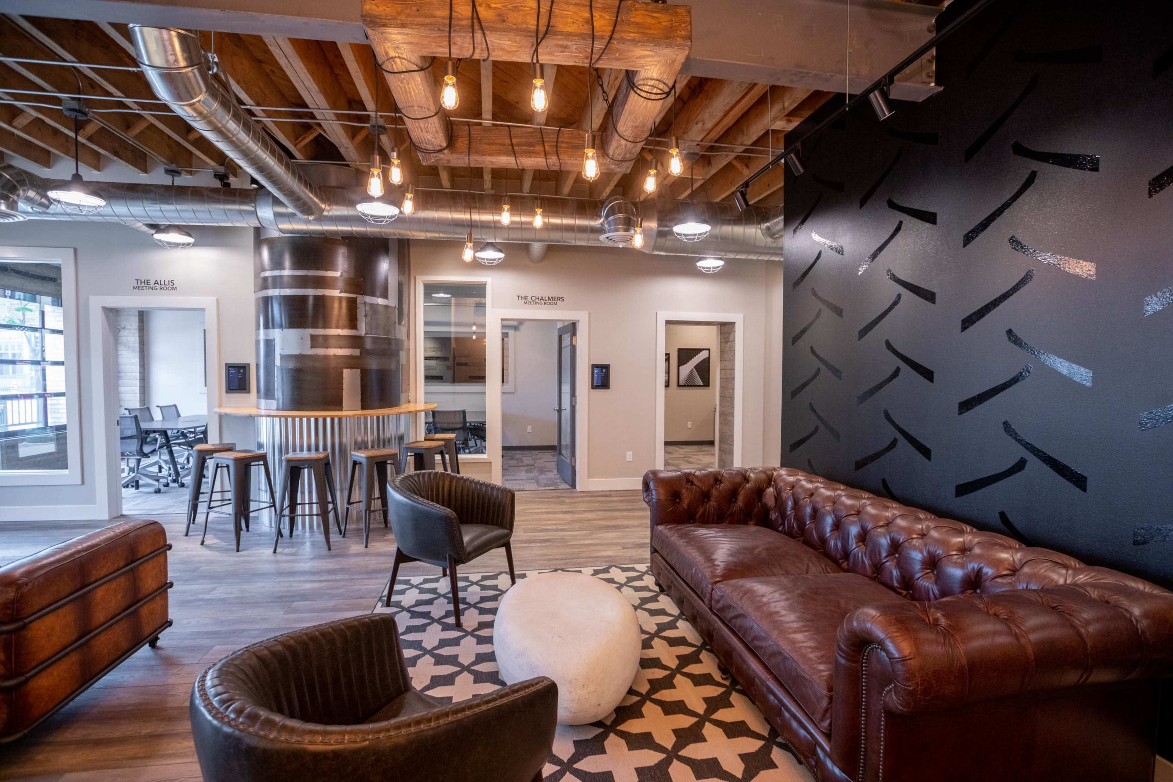 The image features a modern office space with leather furniture, exposed beams, and industrial-style lighting.