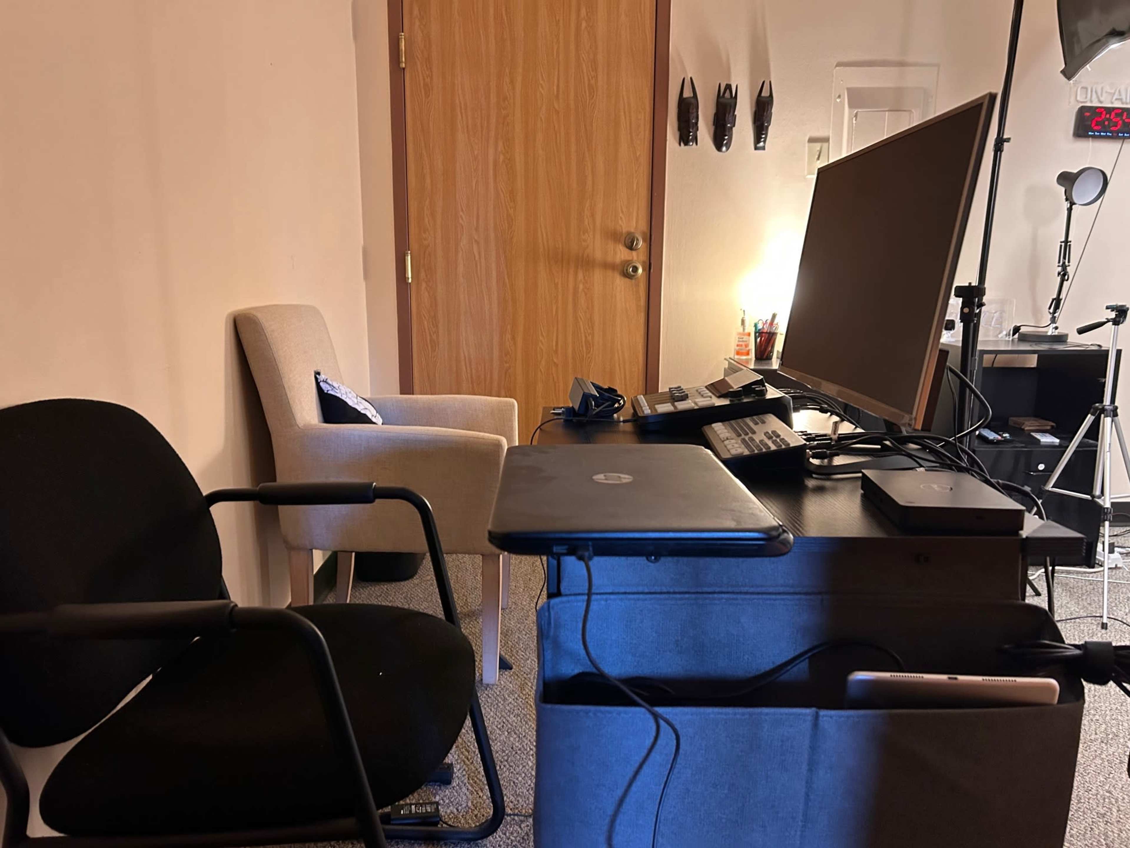 A small workspace featuring a chair, a desk with a computer and accessories, and a lit room in the background.