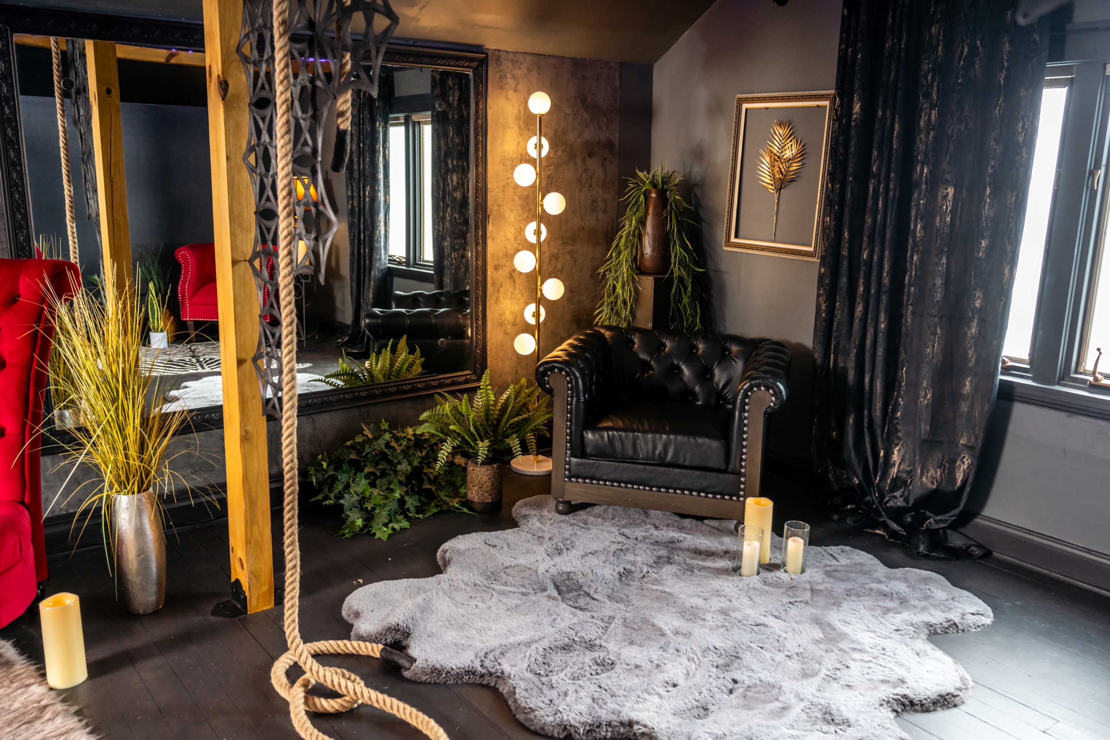 A stylish interior with a black leather armchair, a large mirror, decorative plants, and soft lighting on a textured rug.