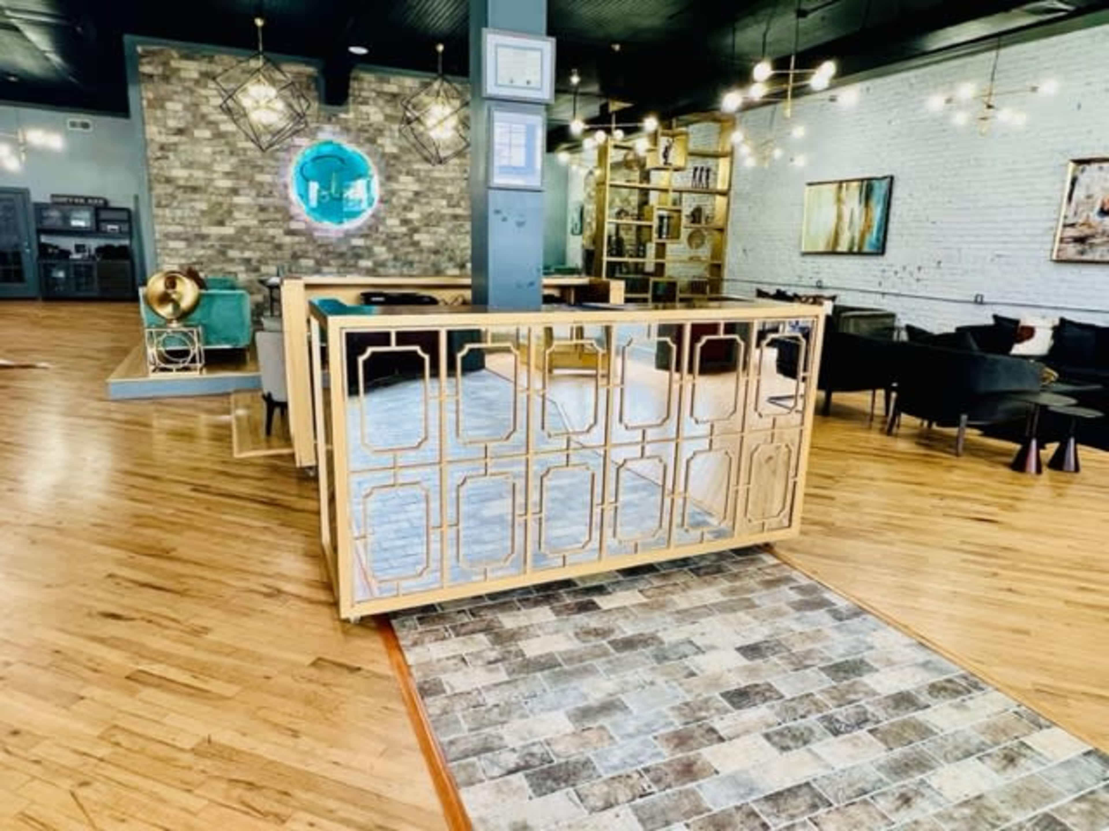 A modern reception area with a mirrored front desk and a wooden floor, framed by stylish decor and seating.