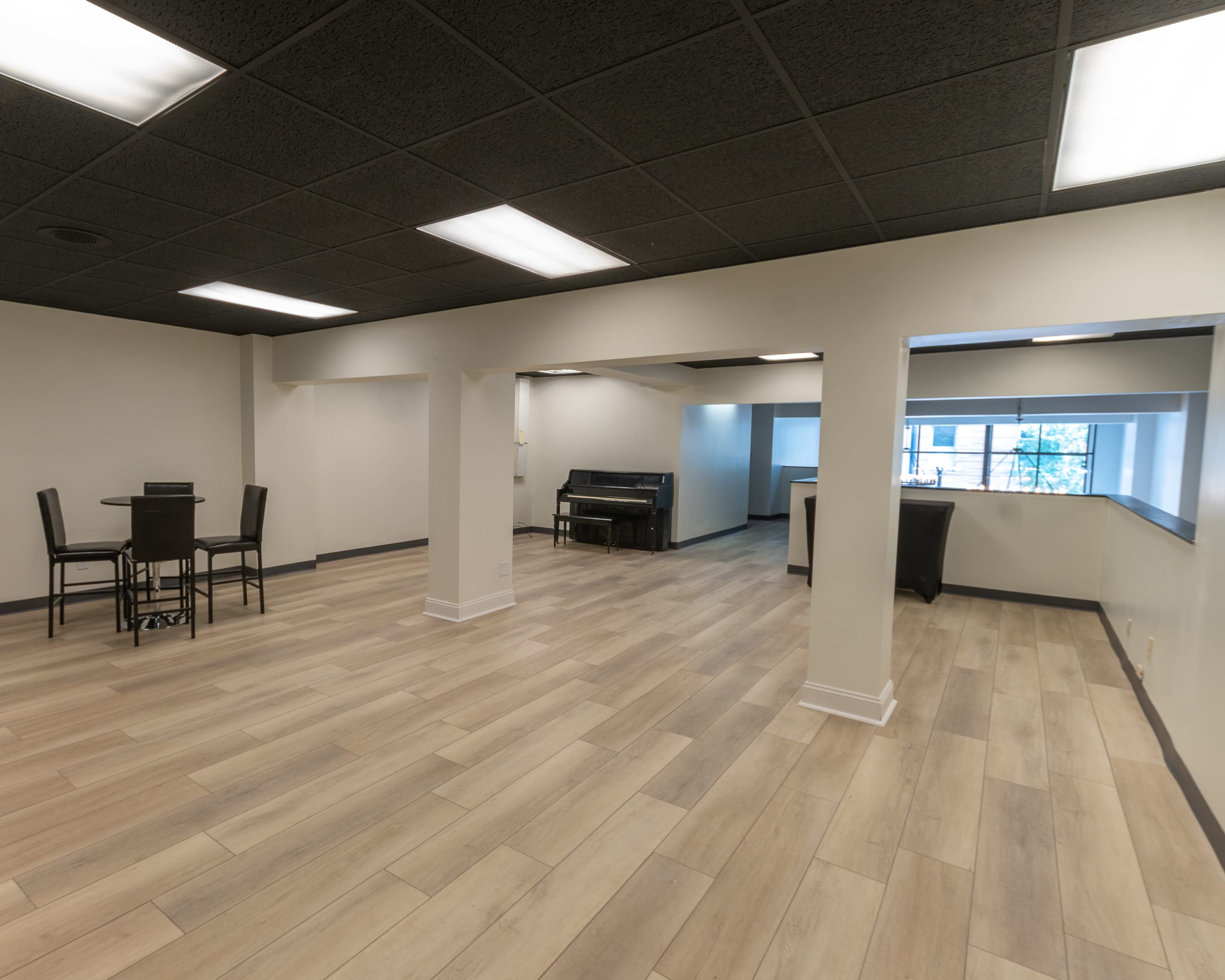 An empty room with wooden flooring, featuring a dining table and chairs on one side and a couch near a window on the other.