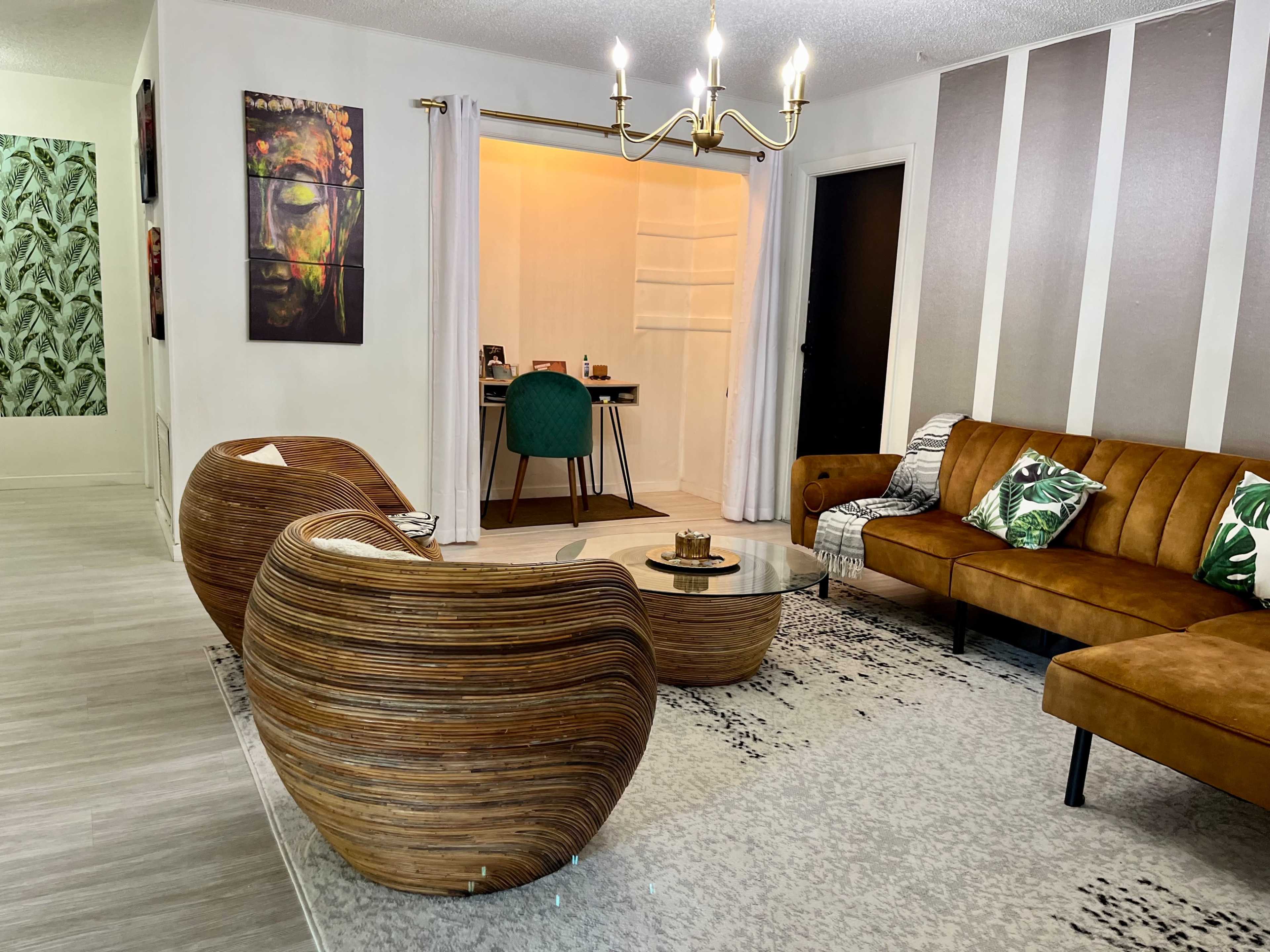 The living room features a wooden coffee table and two curved chairs, with a brown sofa and a desk in the background.