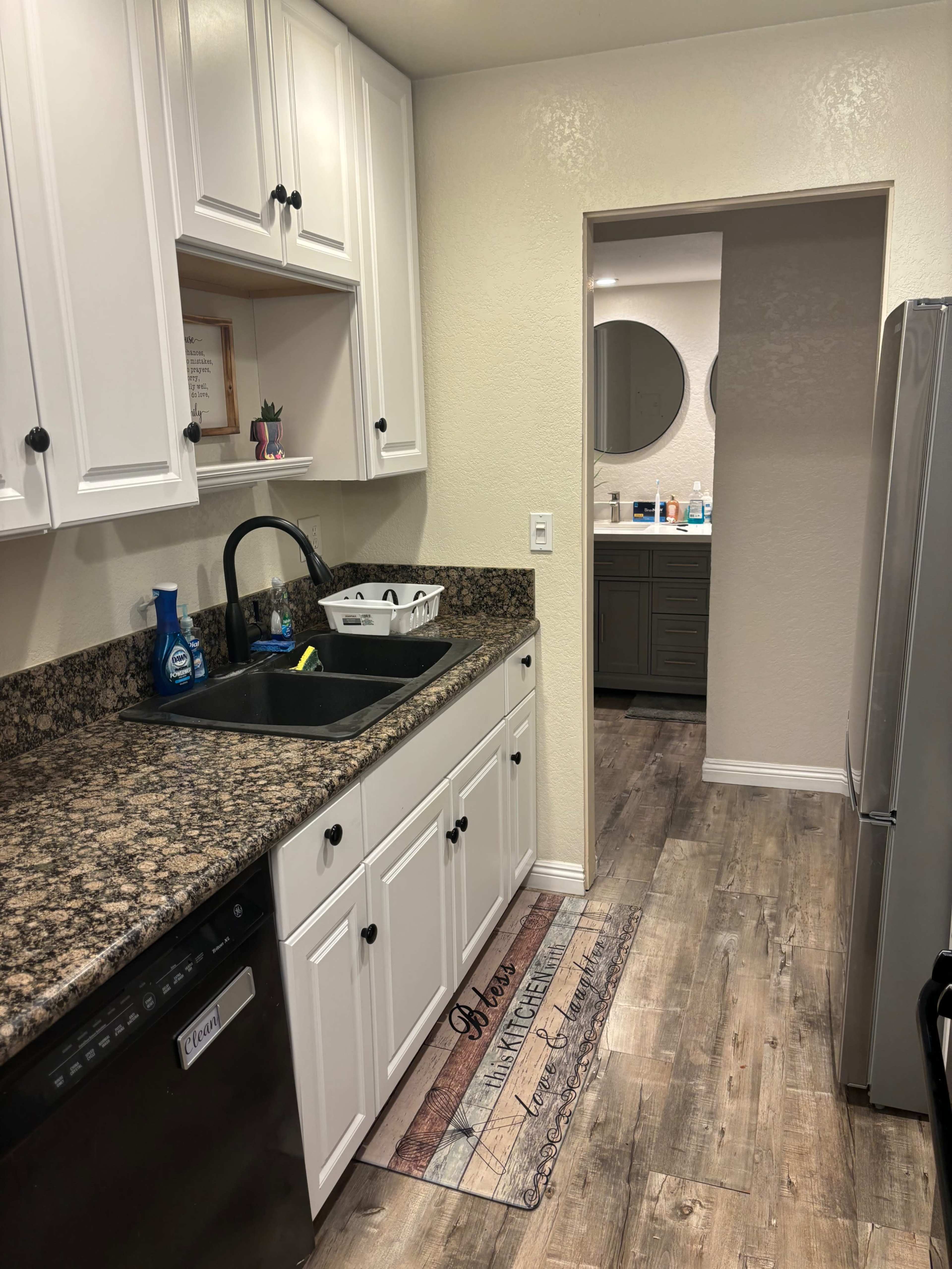 A kitchen with white cabinets, a black sink, and a doorway leading to a bathroom area.