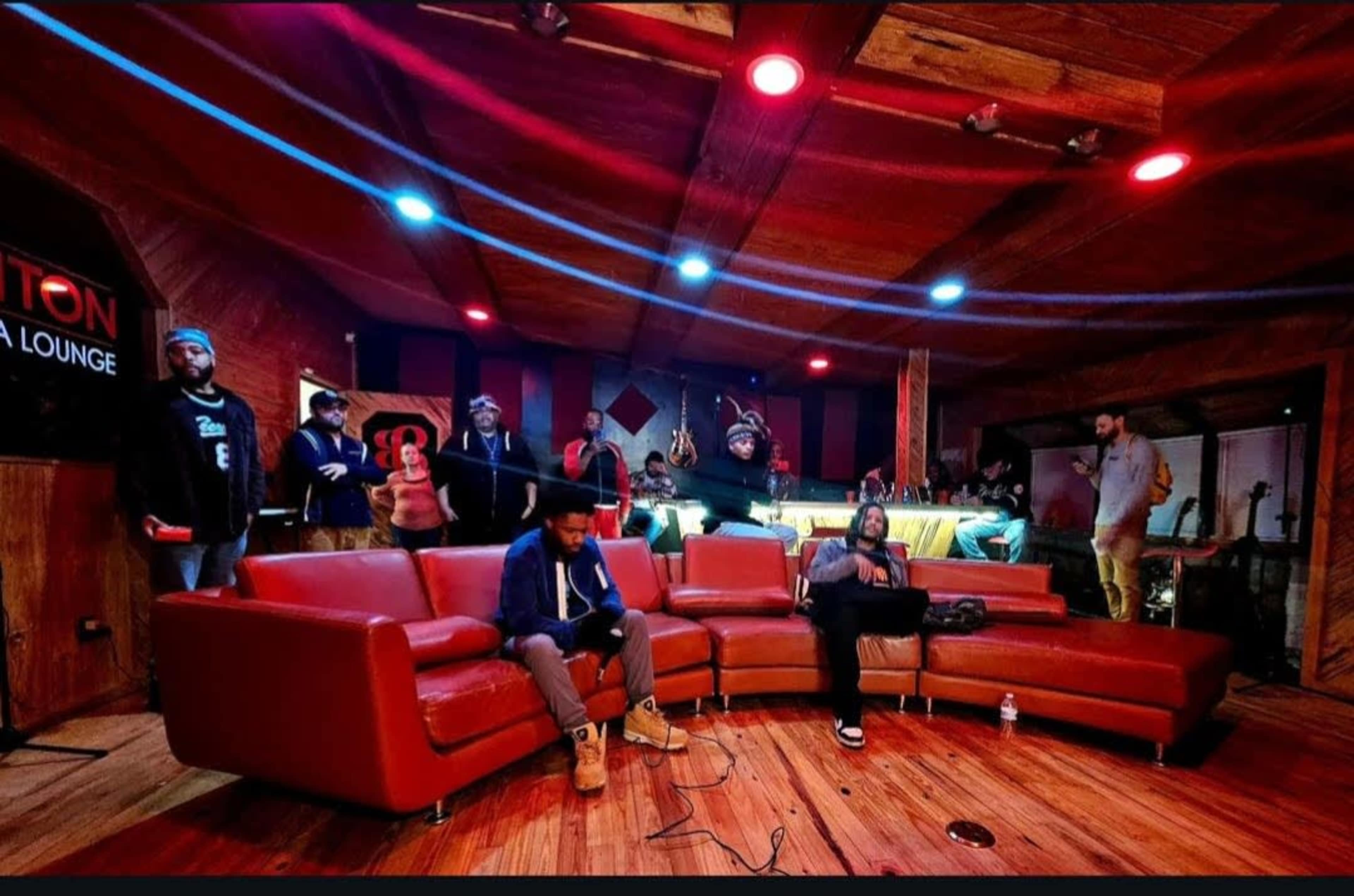 A group of people in a music lounge with a red couch and a performance area in the background.