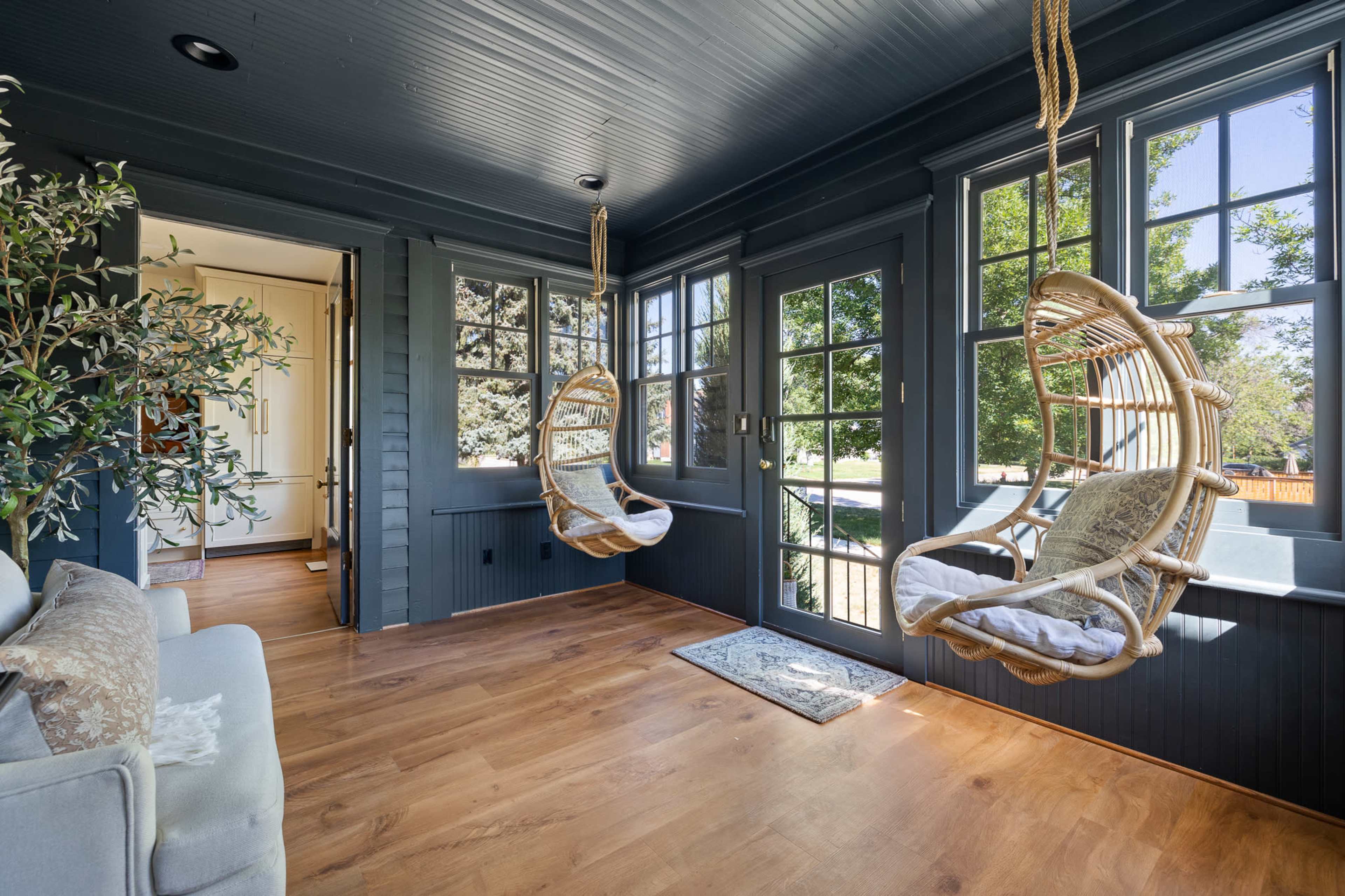 A sunlit room with two hanging rattan chairs positioned near large windows, overlooking a garden.