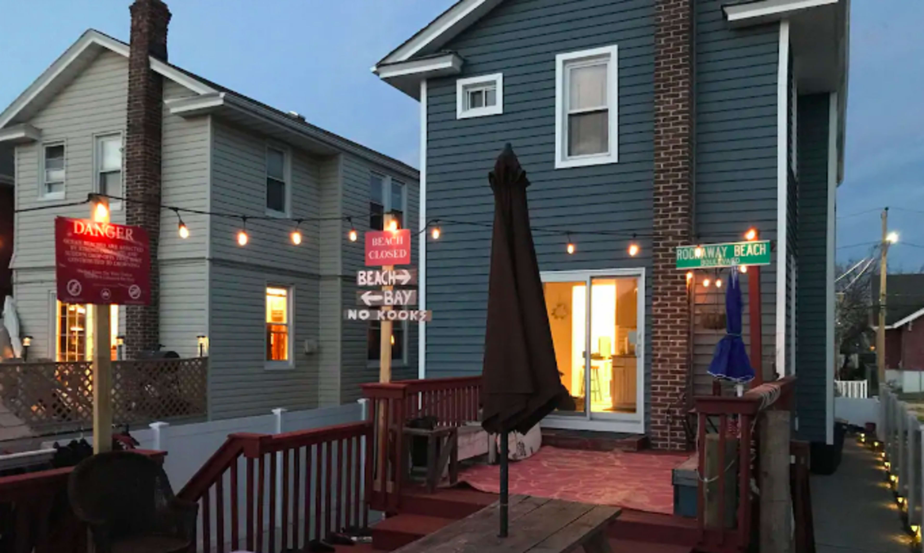 A two-story blue house with a deck and string lights, featuring a closed sign and street signs pointing to Beach and Rocky Beach.