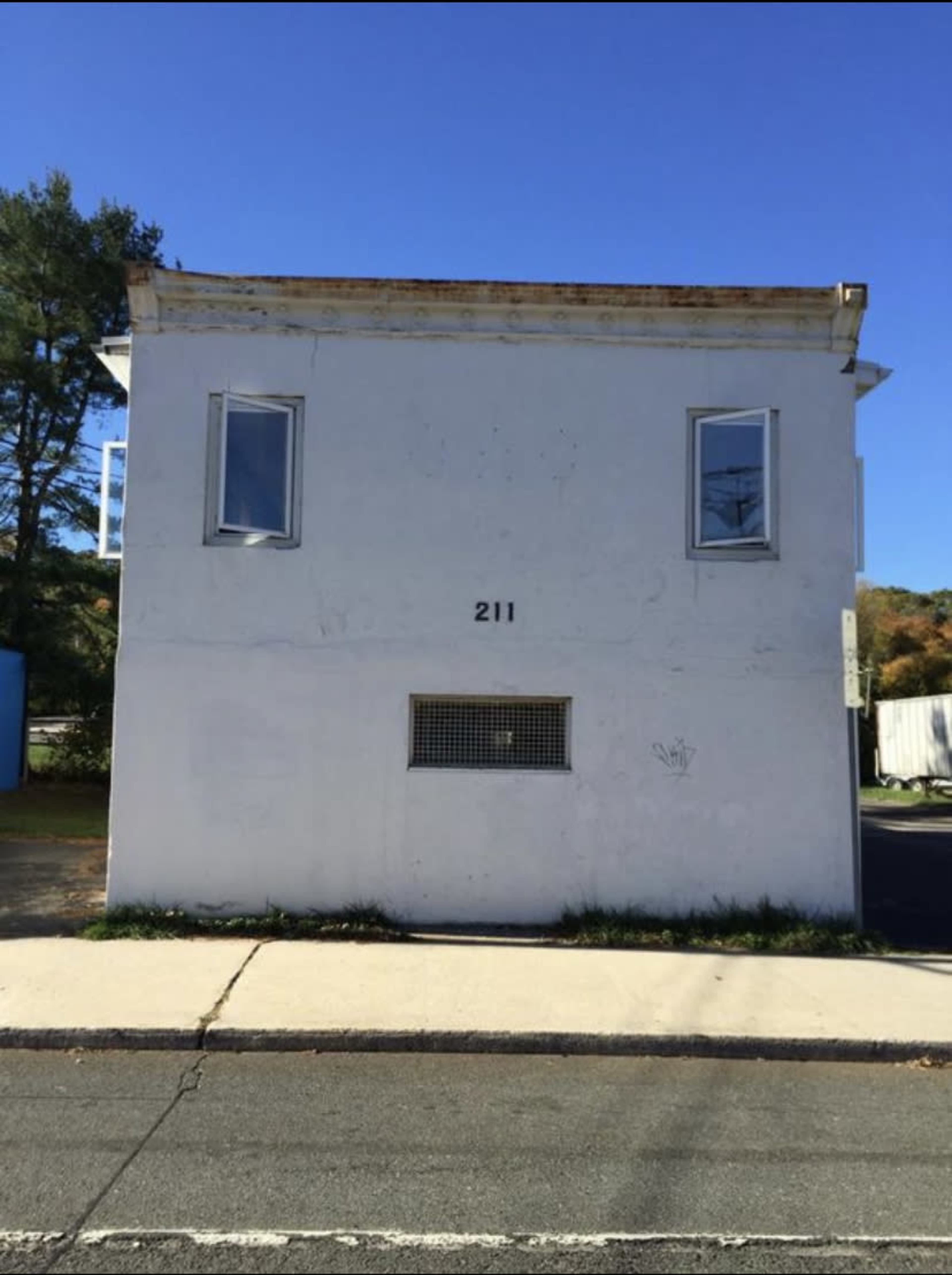 A two-story white building with the number 211 displayed on its front facade, situated next to a road.