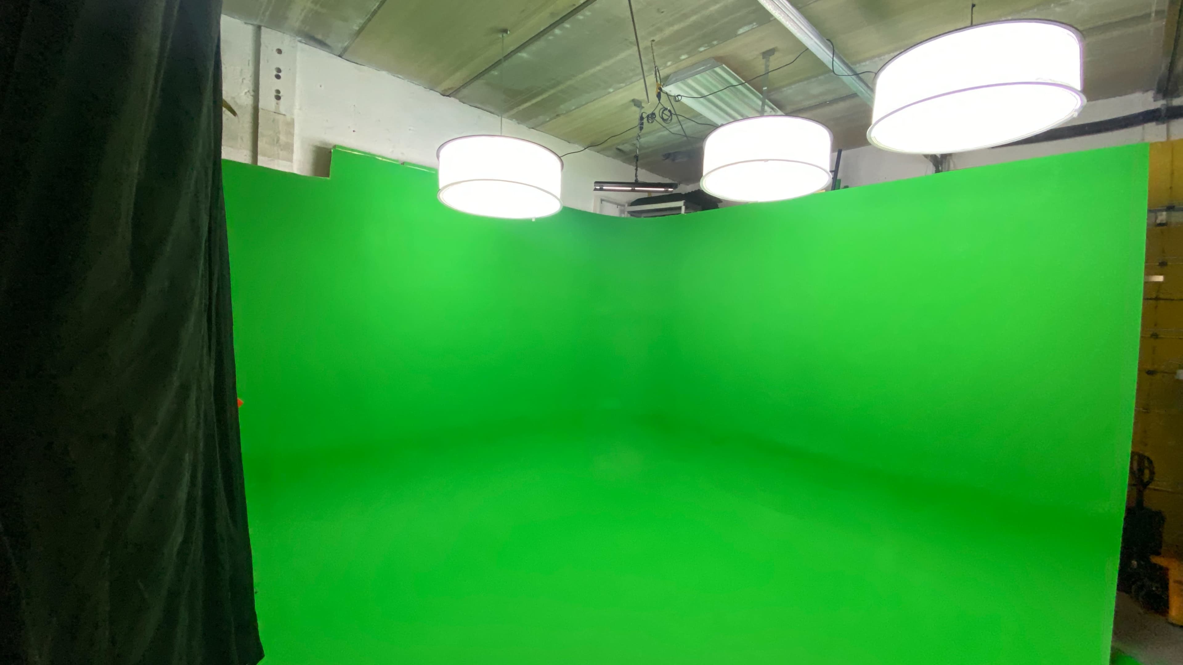 A green screen studio with three round pendant lights hanging from the ceiling.