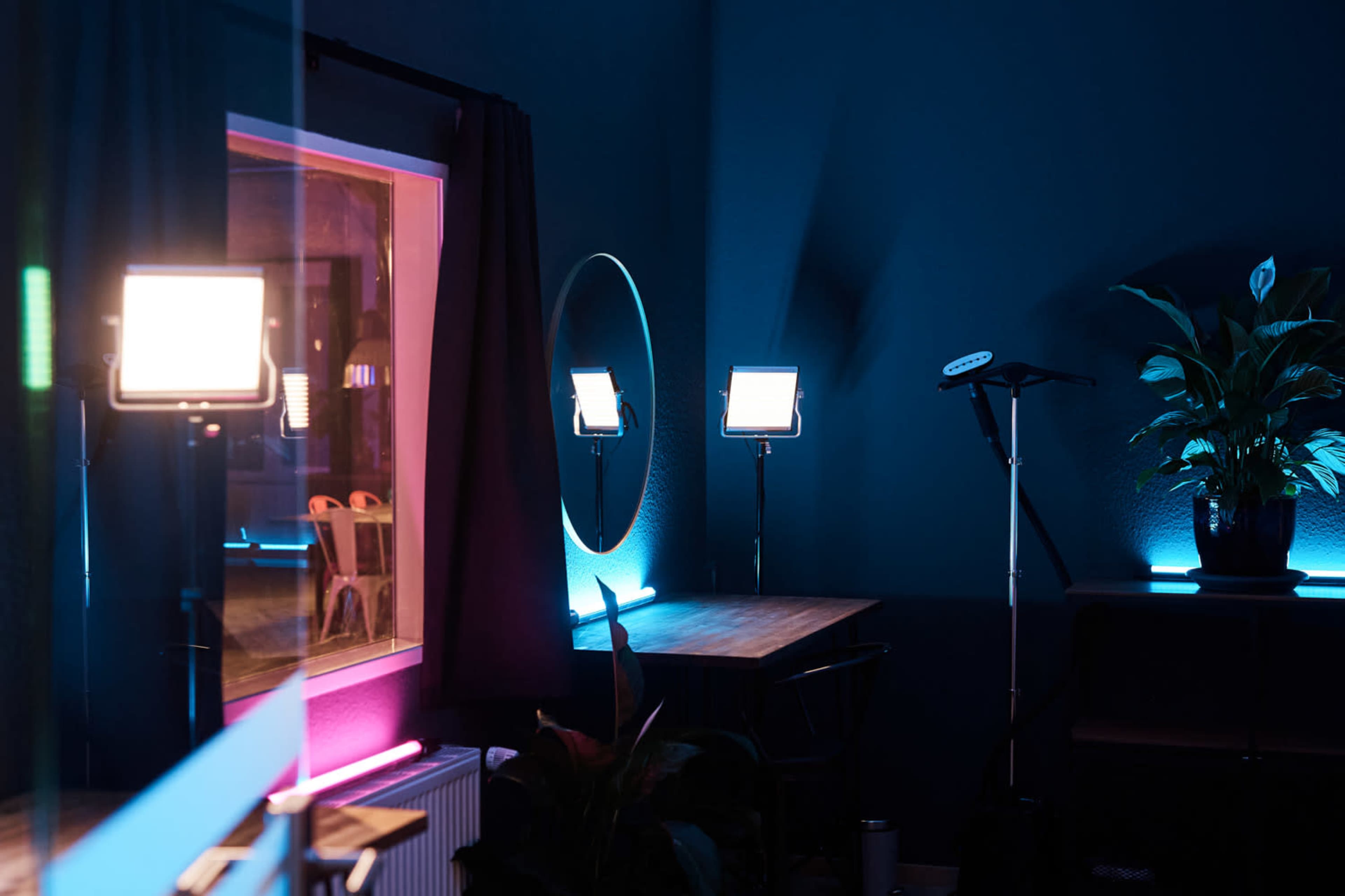 The image depicts a dimly lit room with various lighting setups, including a mirror and a plant, arranged around a wooden table.