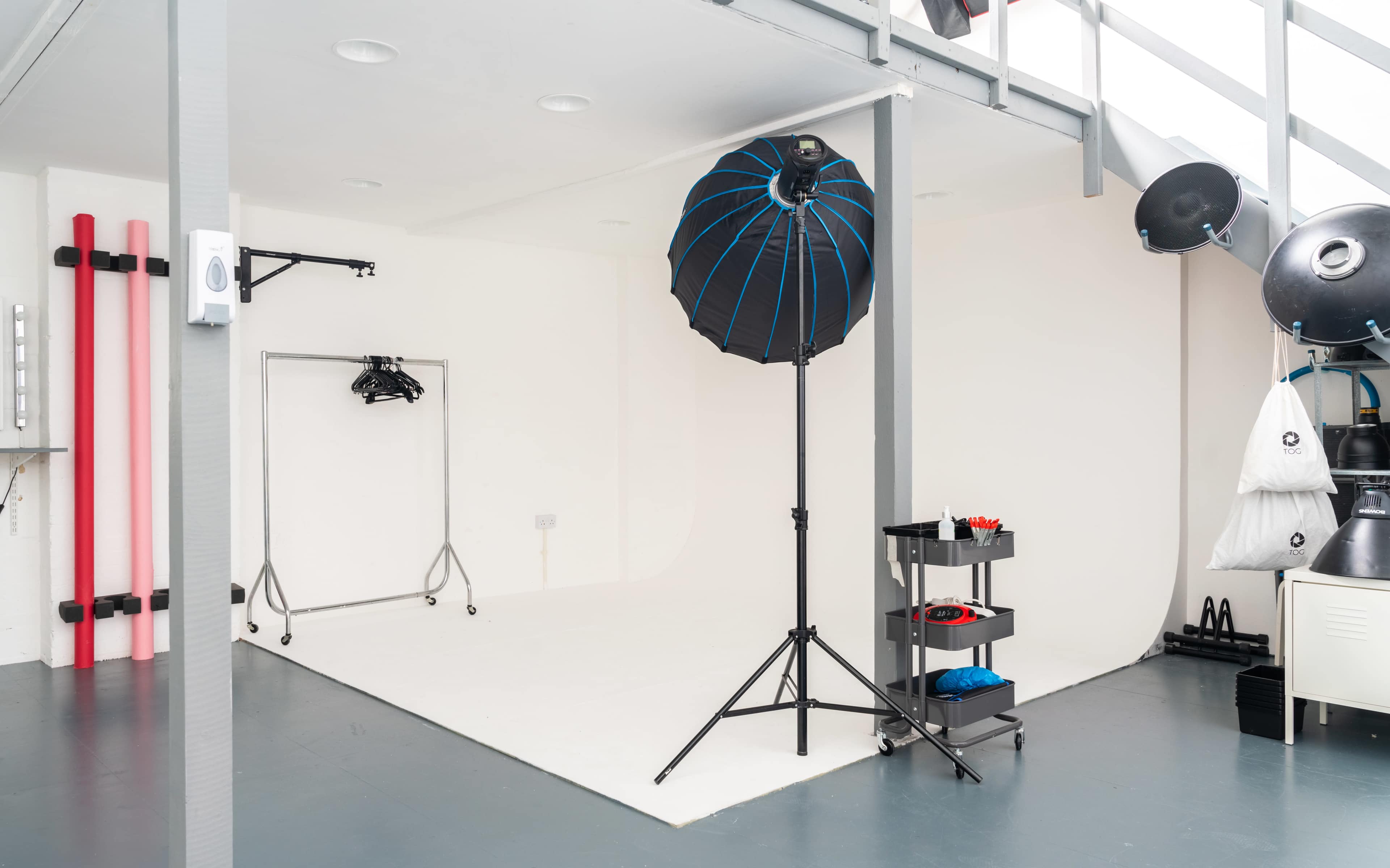 A photography studio with a white backdrop, lighting equipment, and a clothing rack.