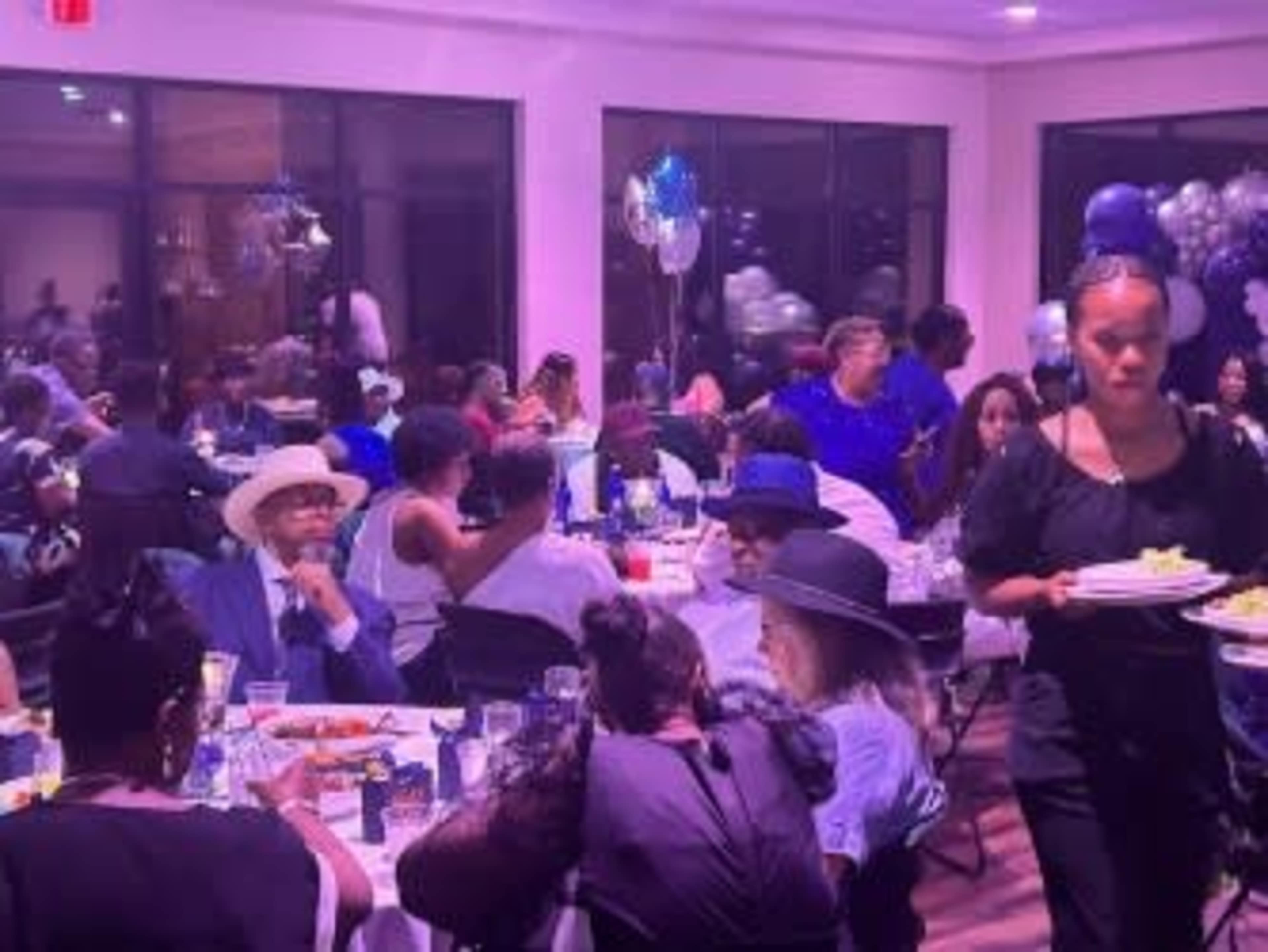 A crowded dining hall is filled with guests seated at tables, while a waitress serves food.