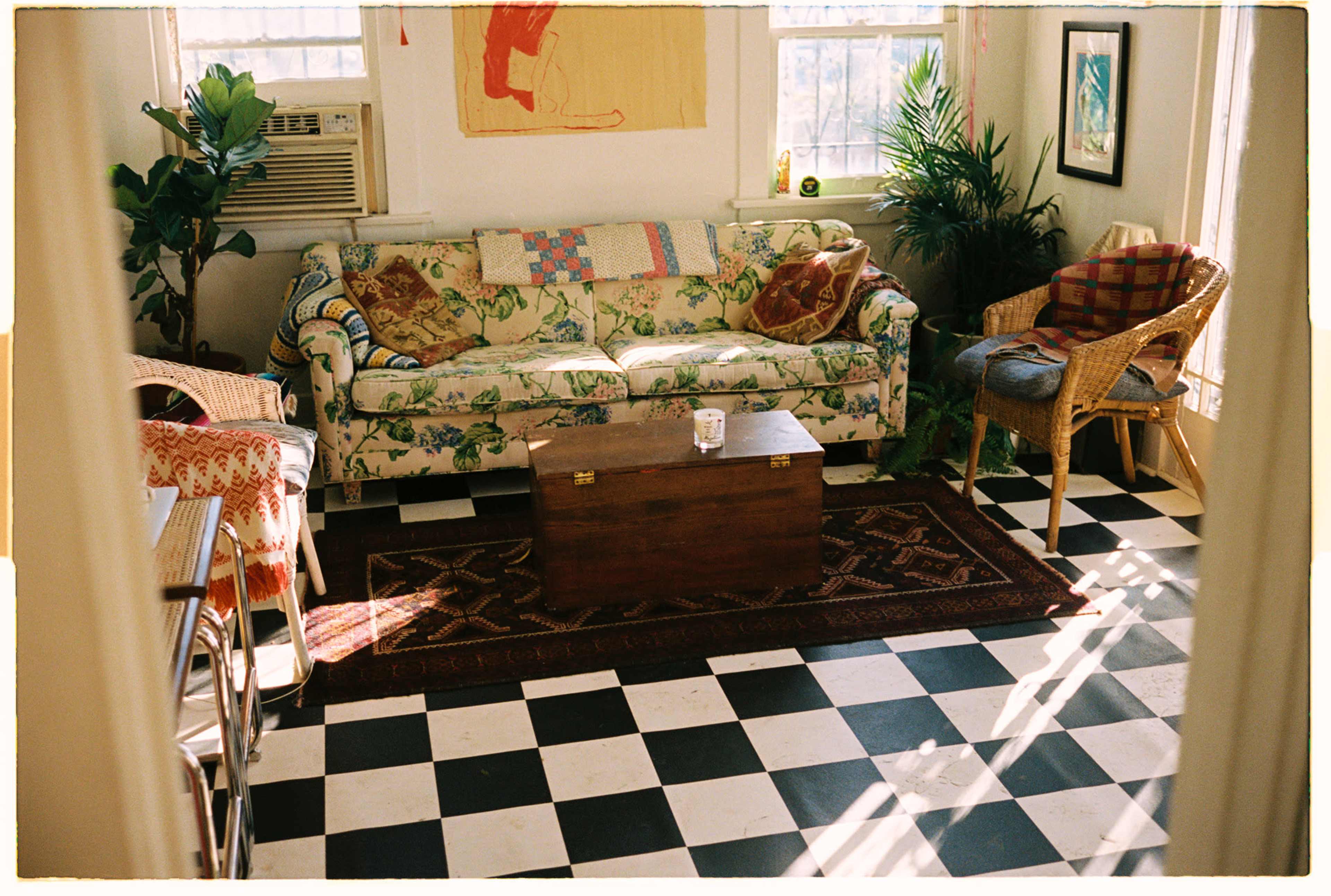 The image depicts a cozy living room featuring a patterned couch, a wooden coffee table, and various armchairs arranged around a checkered floor.
