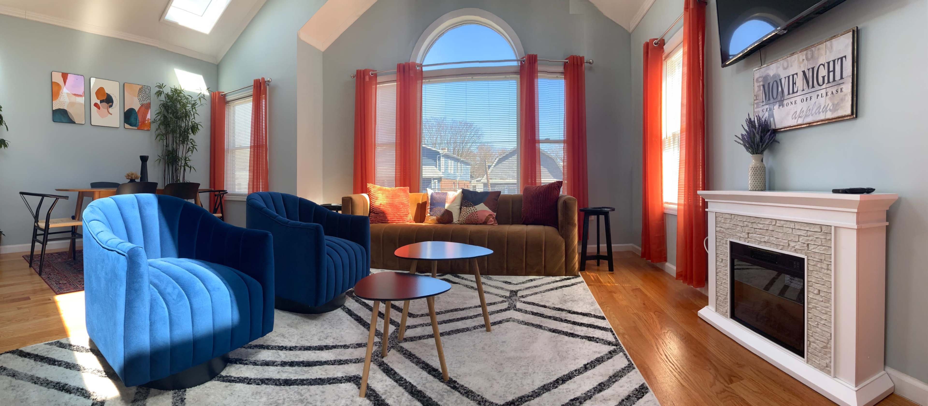 A spacious living room with a blue and brown seating arrangement, large windows, and a modern fireplace.