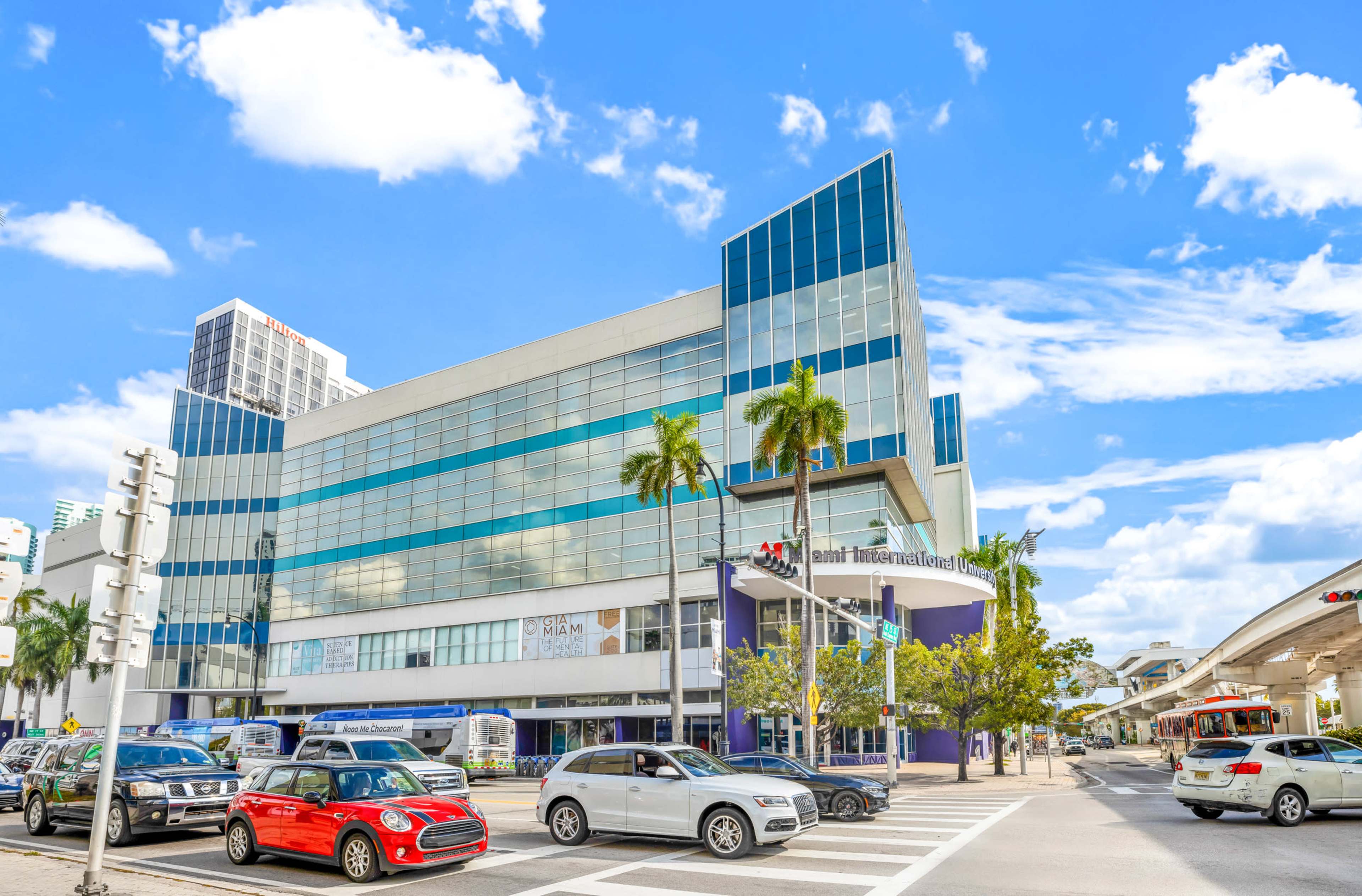 A modern building with large glass windows and palm trees is situated at a busy intersection in an urban area.
