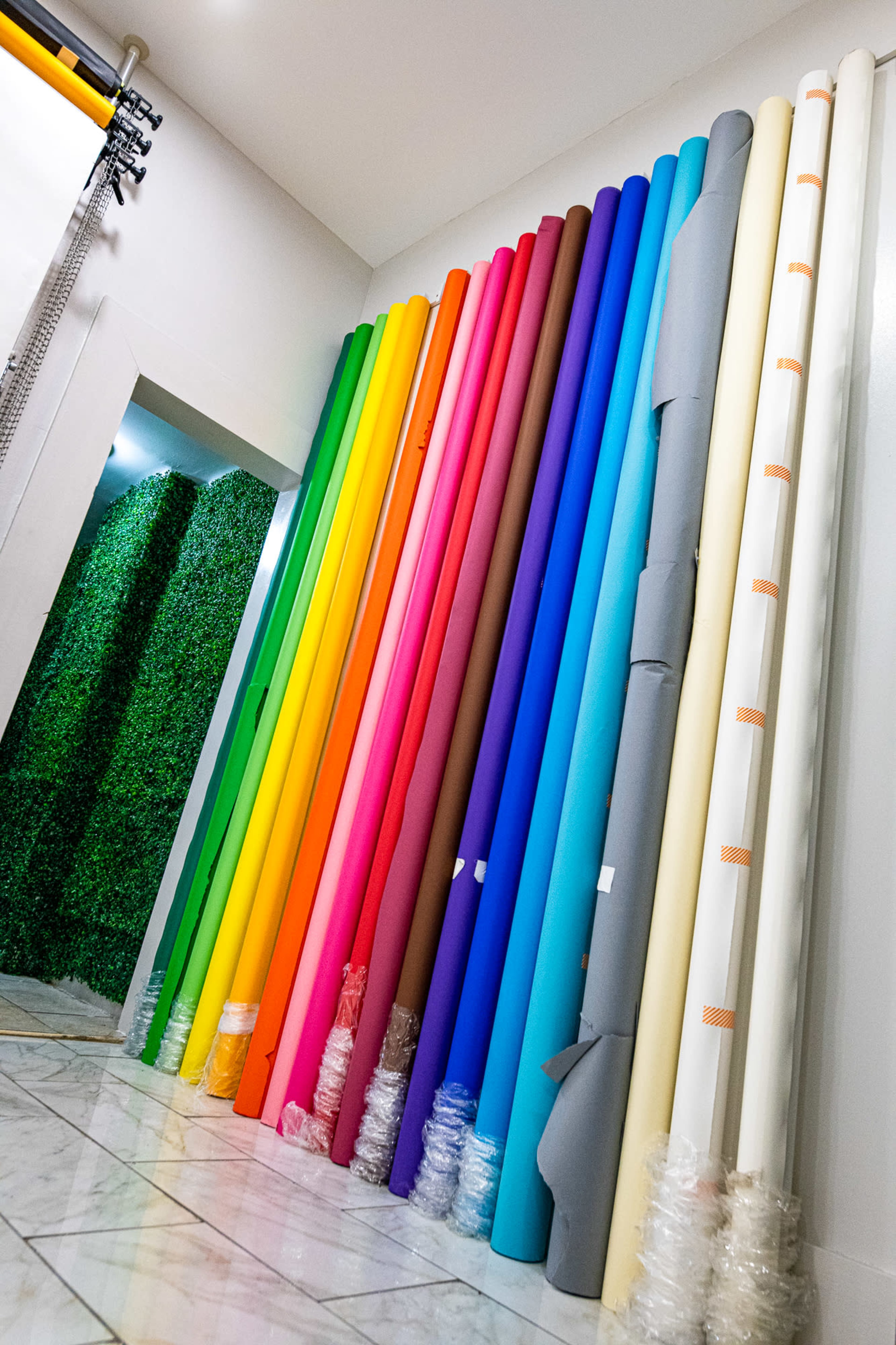 A colorful array of rolled-backdrops arranged vertically along a wall in a room with tiled flooring.
