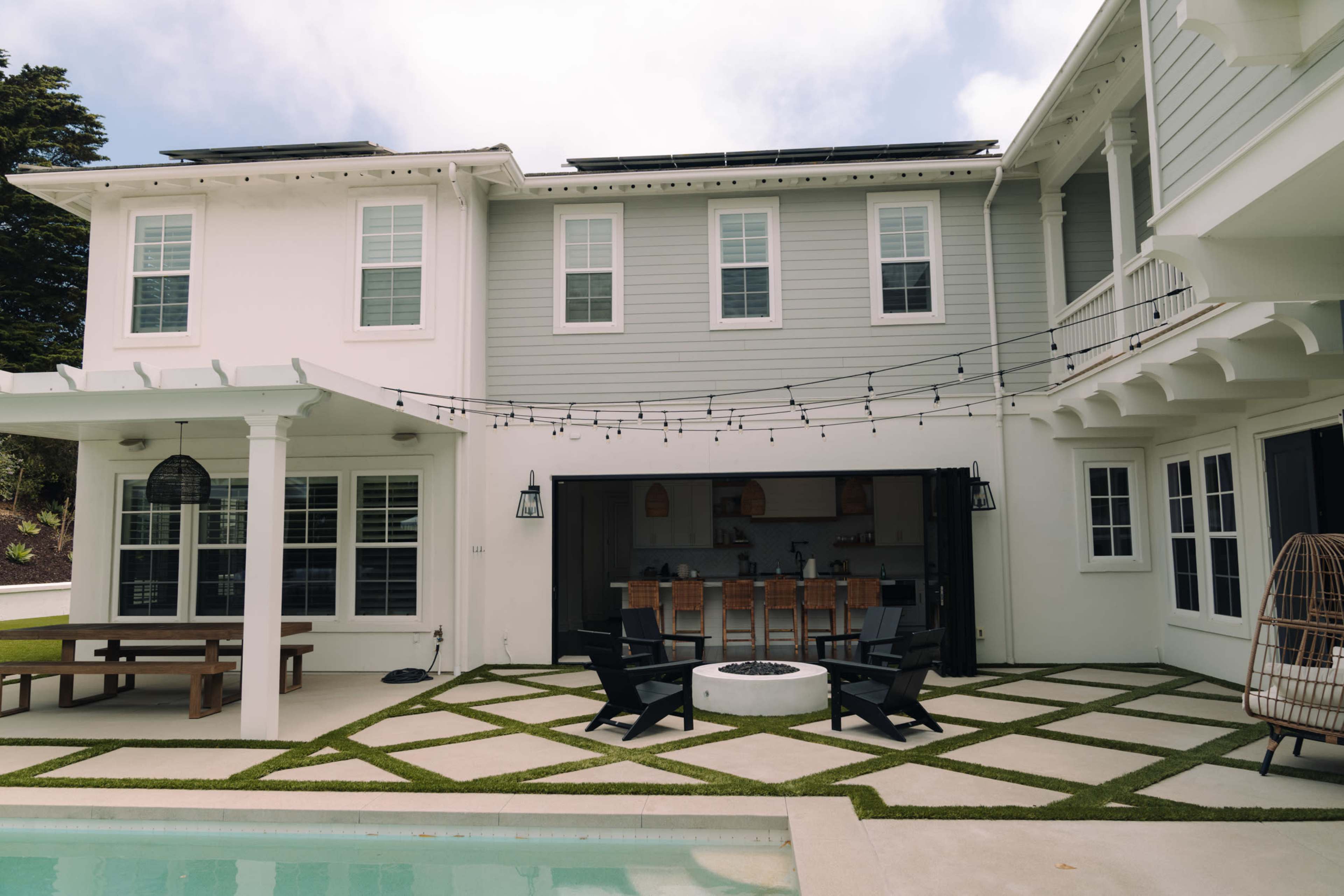 A modern two-story house features a spacious outdoor area with a patio, fire pit, and string lights.