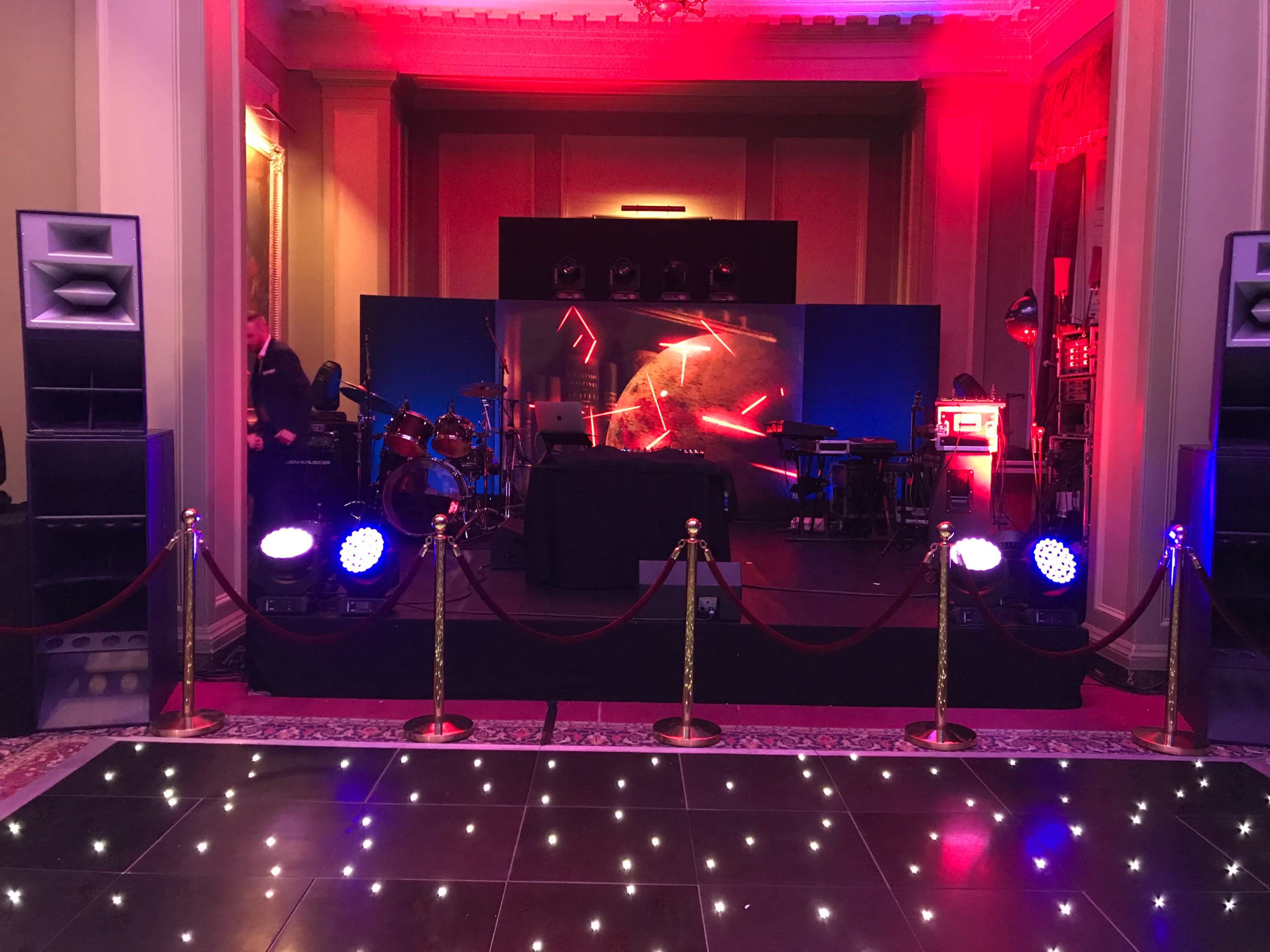 The scene features a stage set up for a performance, with a sound system, musical instruments, and decorative lighting in a spacious room.