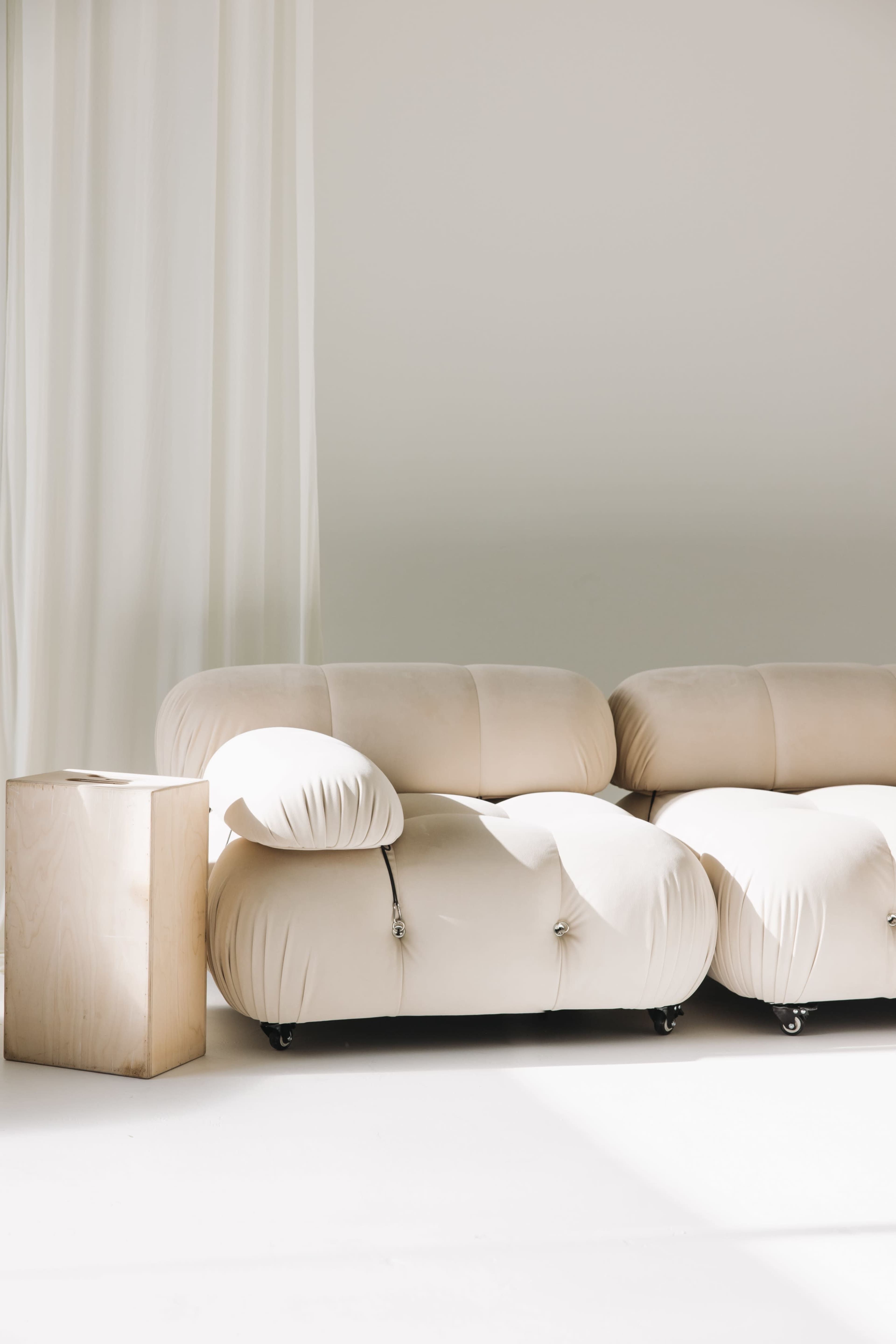 The image features a light-colored, curvy sofa next to a simple wooden side table in a bright, minimalistic room with soft natural light.